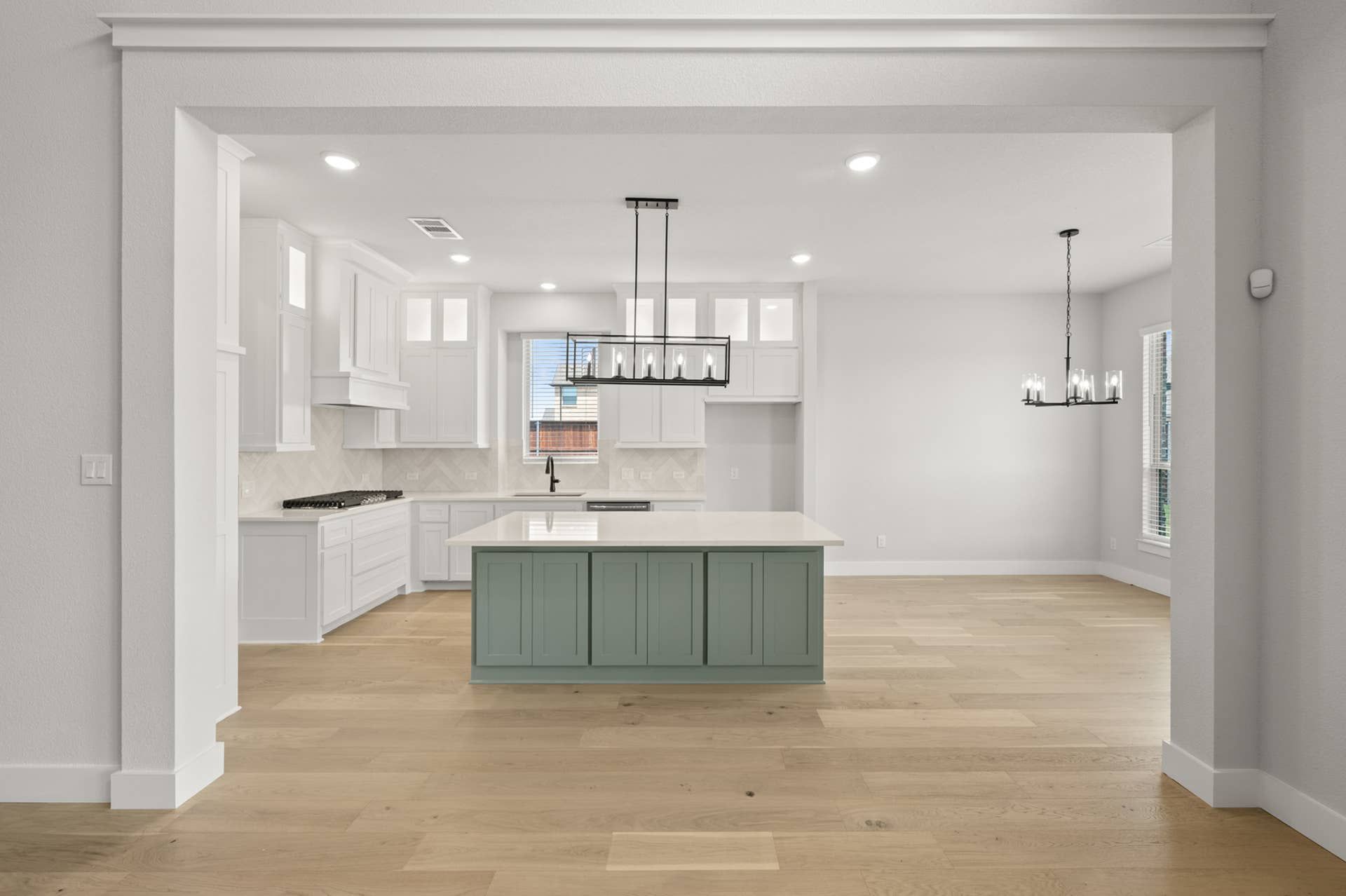 Modern kitchen with green island, wood floors, and elegant lighting fixtures.