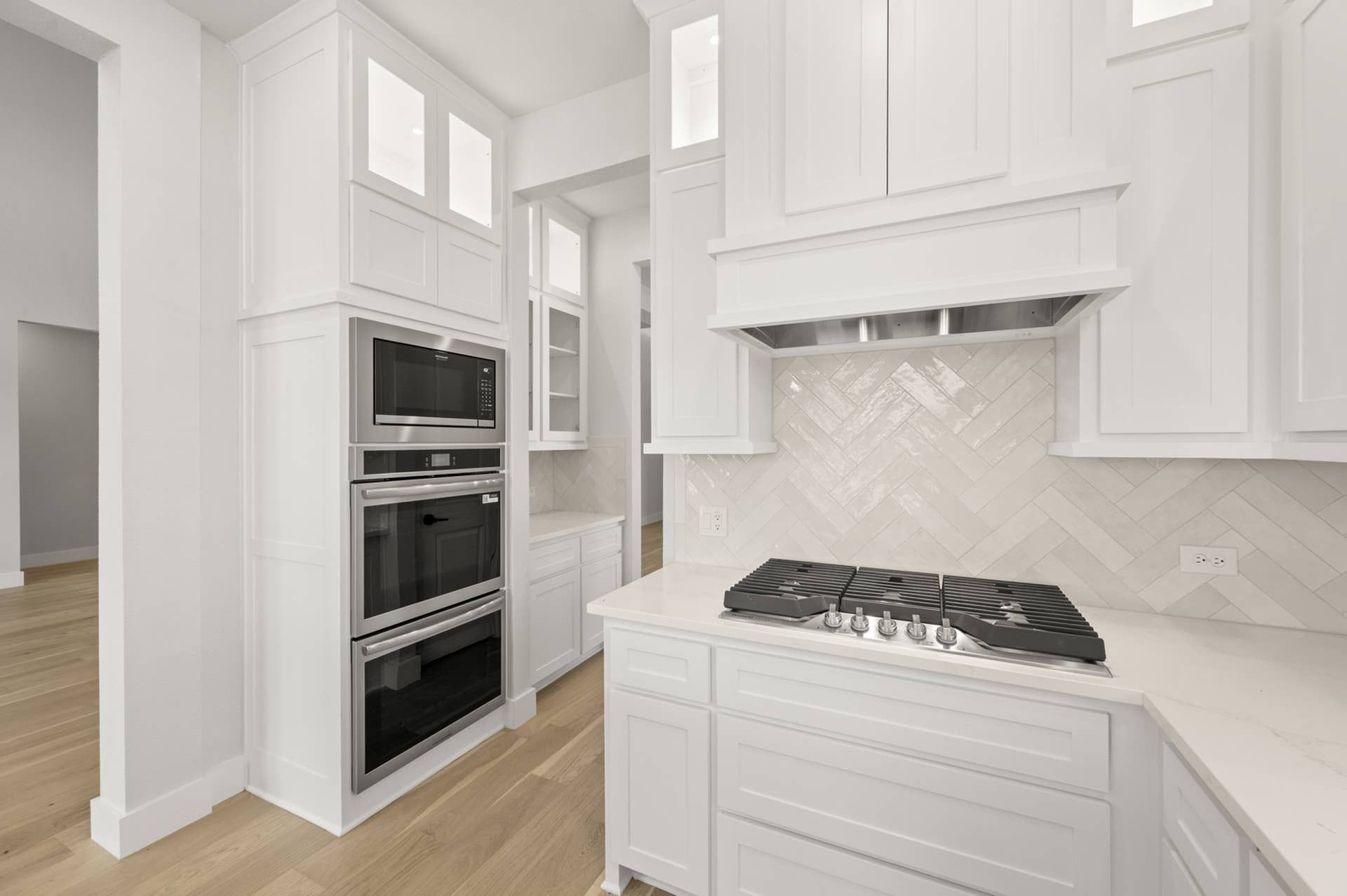 Modern kitchen with white cabinetry, built-in microwave, and herringbone backsplash.