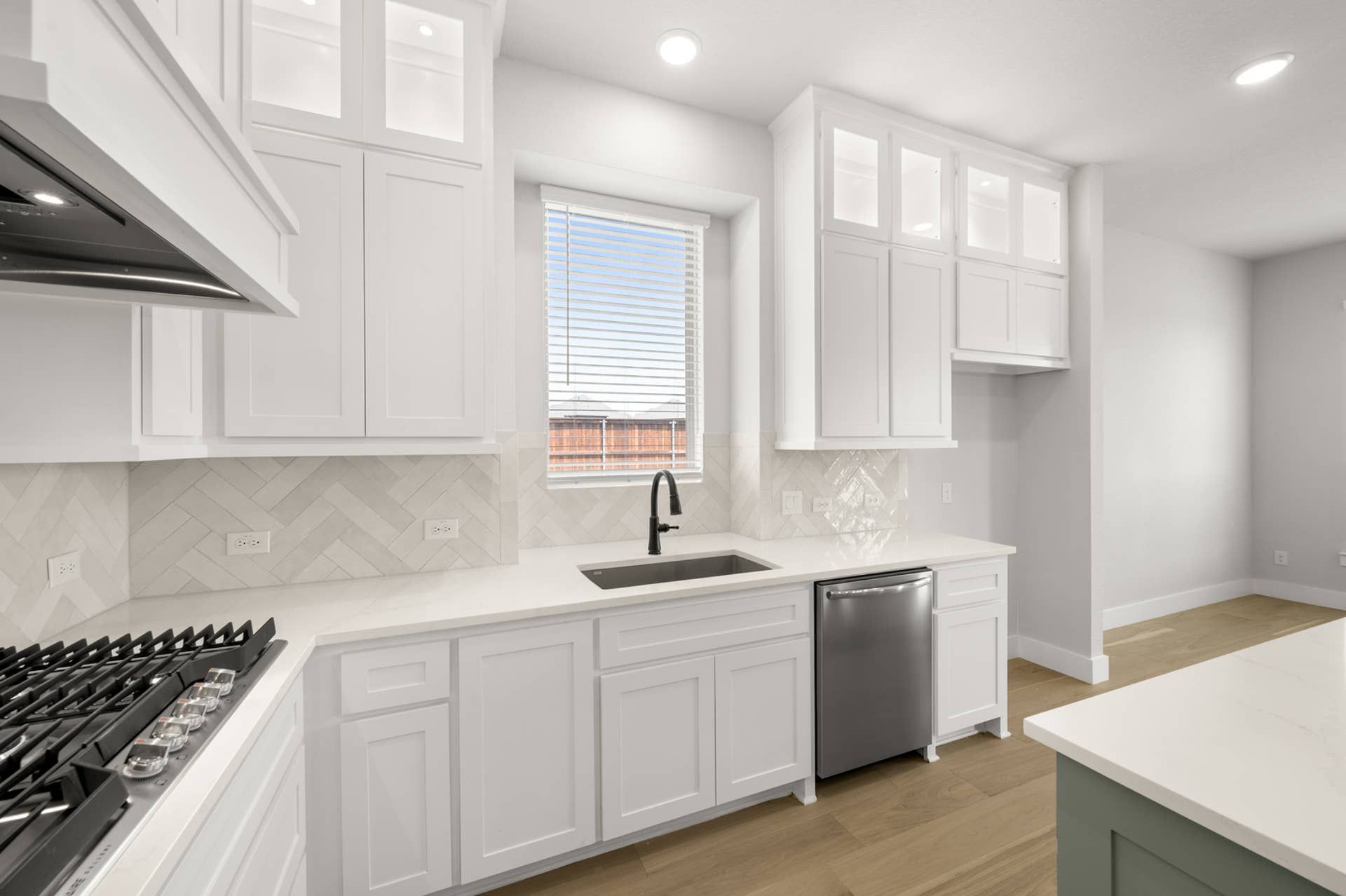 Modern kitchen with white cabinetry, herringbone backsplash, and stainless steel appliances.
