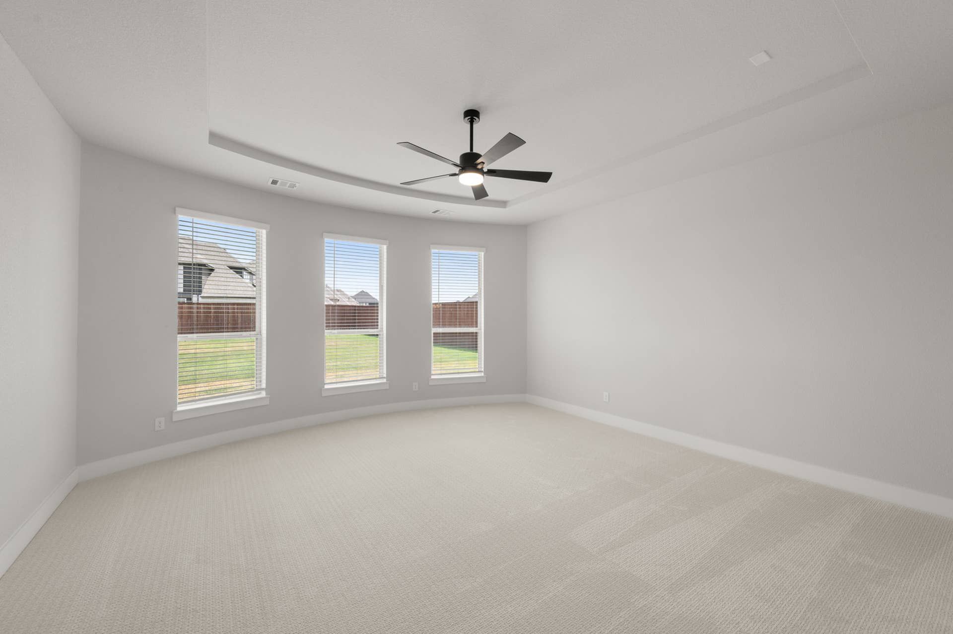 Spacious primary suite with ceiling fan and large windows overlooking backyard.