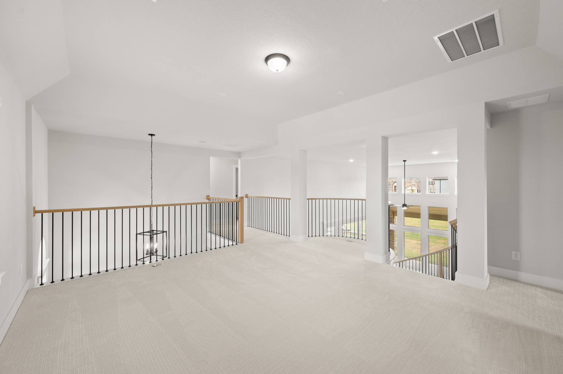 Spacious bright game room with modern railing and plush carpeting.