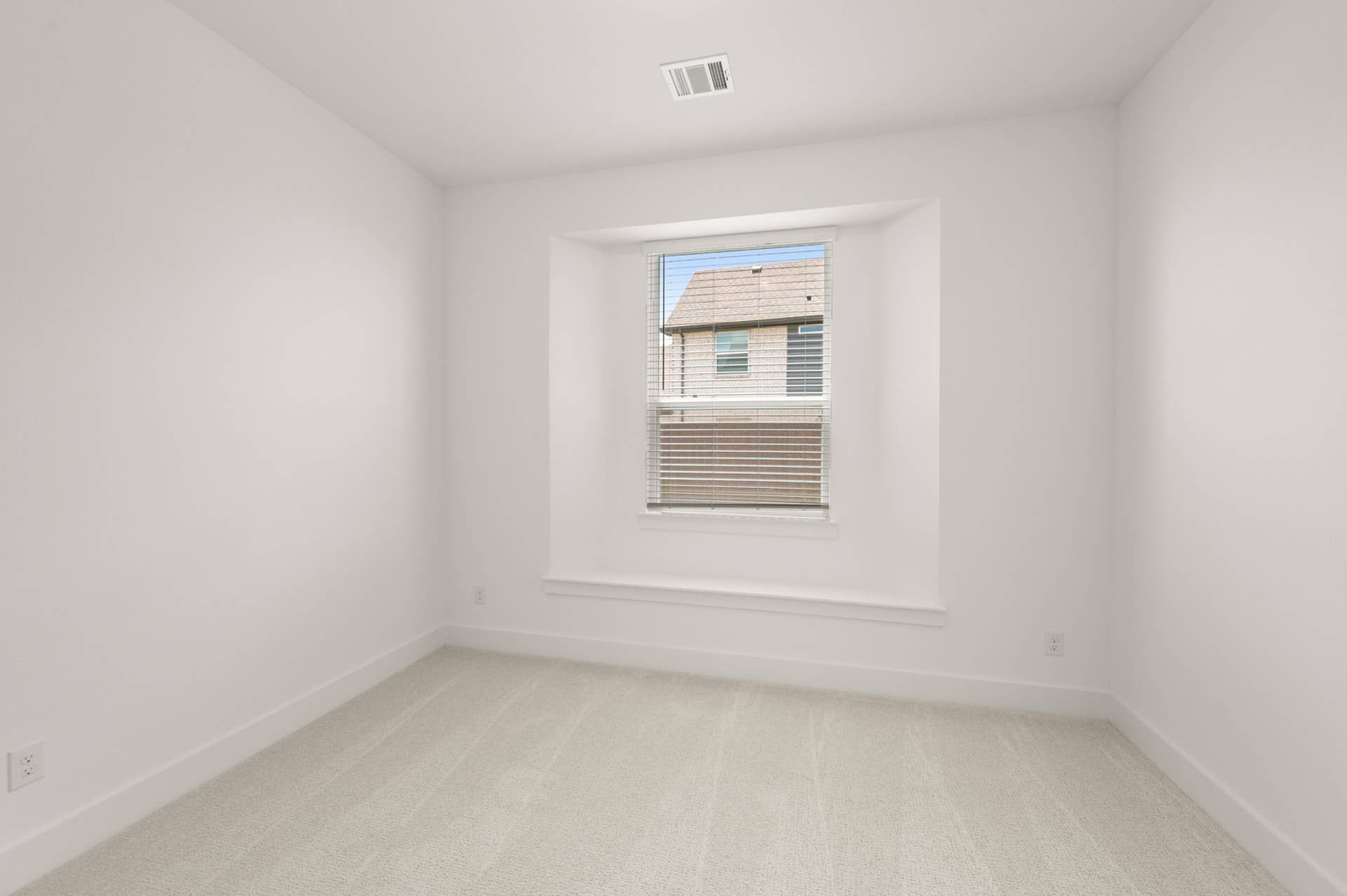 Bright study room with white walls and carpet, featuring a large window.
