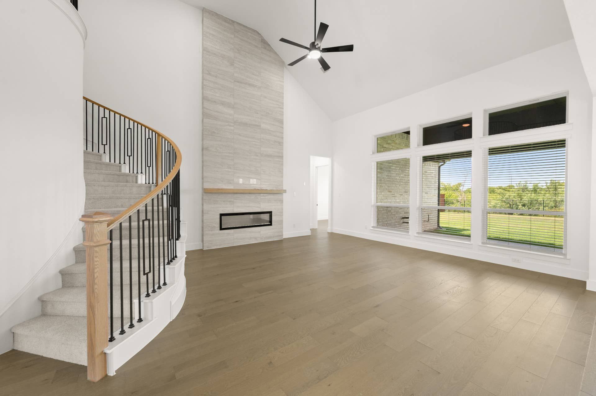 Spacious living room with modern fireplace, curved staircase, and large windows.