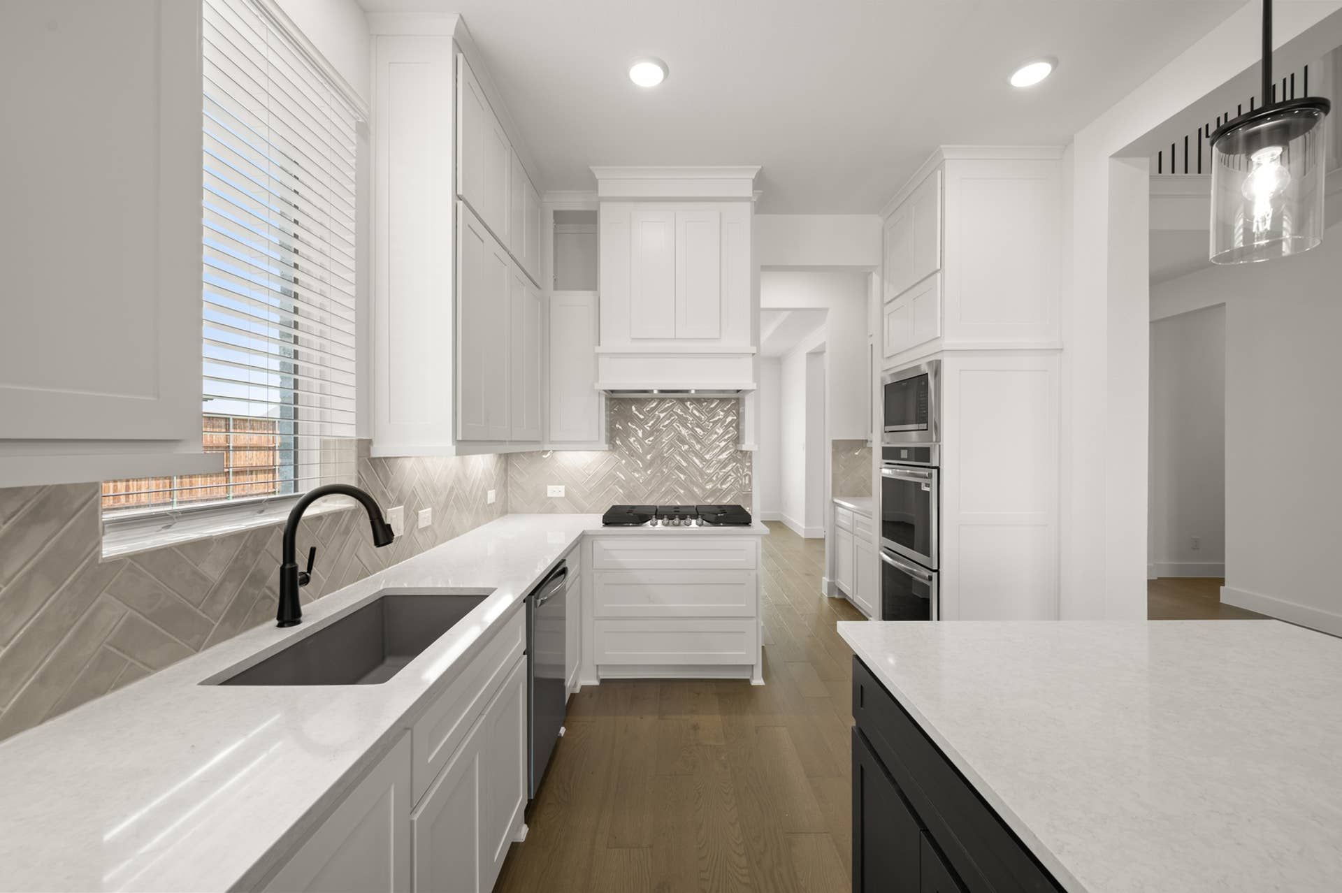 Modern kitchen with white cabinetry, marble countertops, and herringbone tile backsplash.