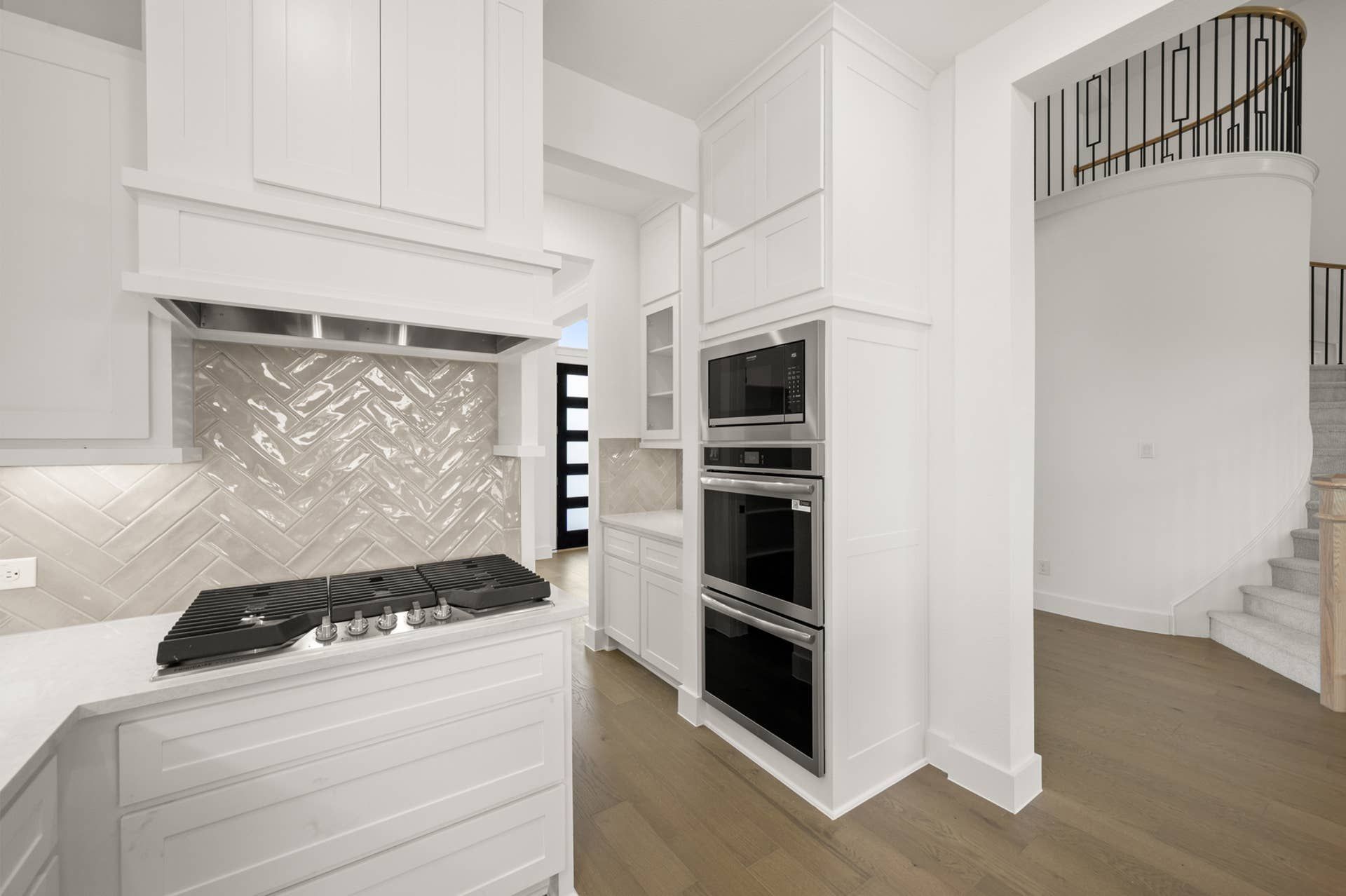 Modern kitchen with herringbone backsplash, white cabinetry, and integrated double oven.