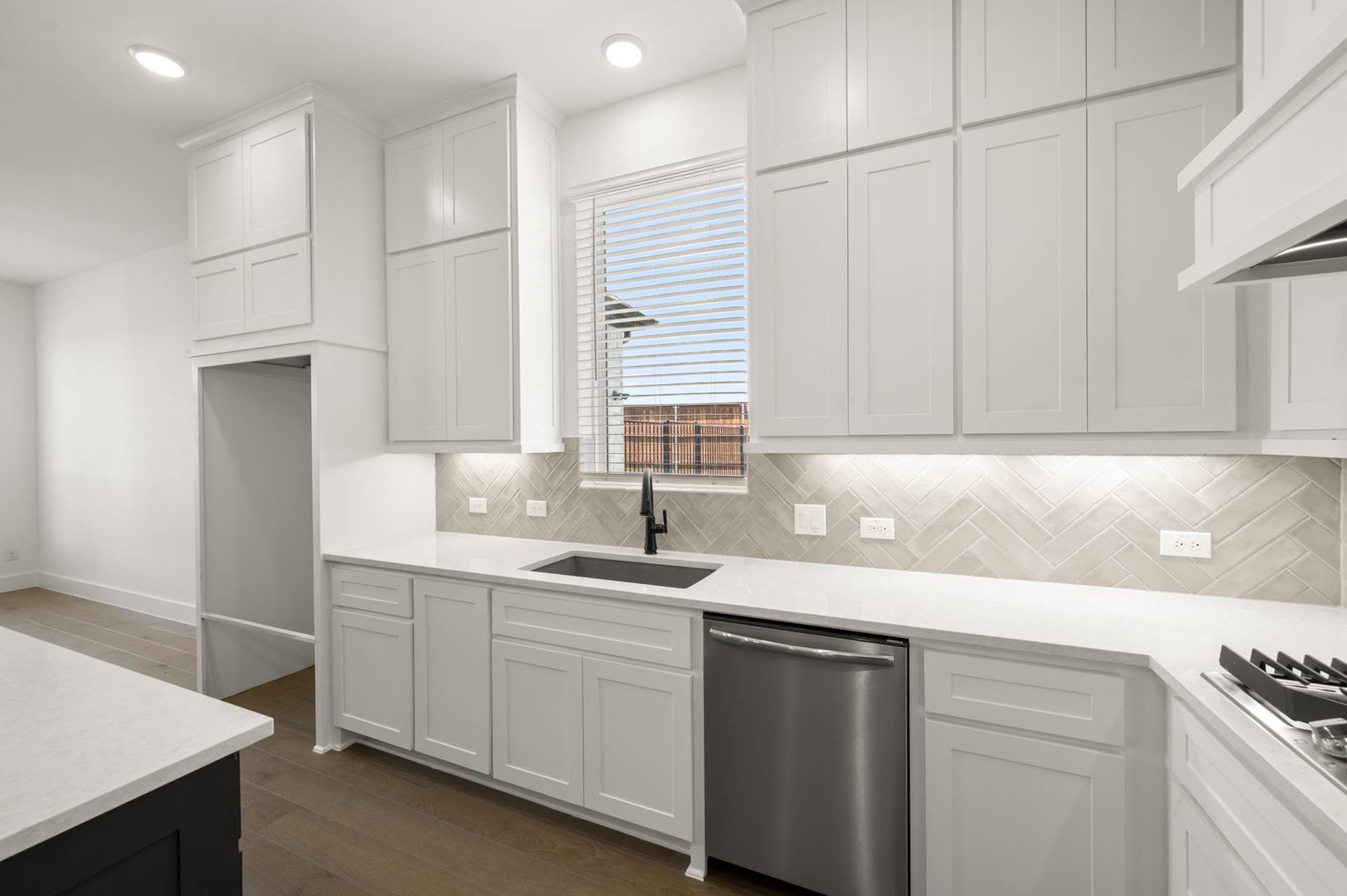 Modern kitchen with white cabinetry, stainless steel appliances, and herringbone tile backsplash.