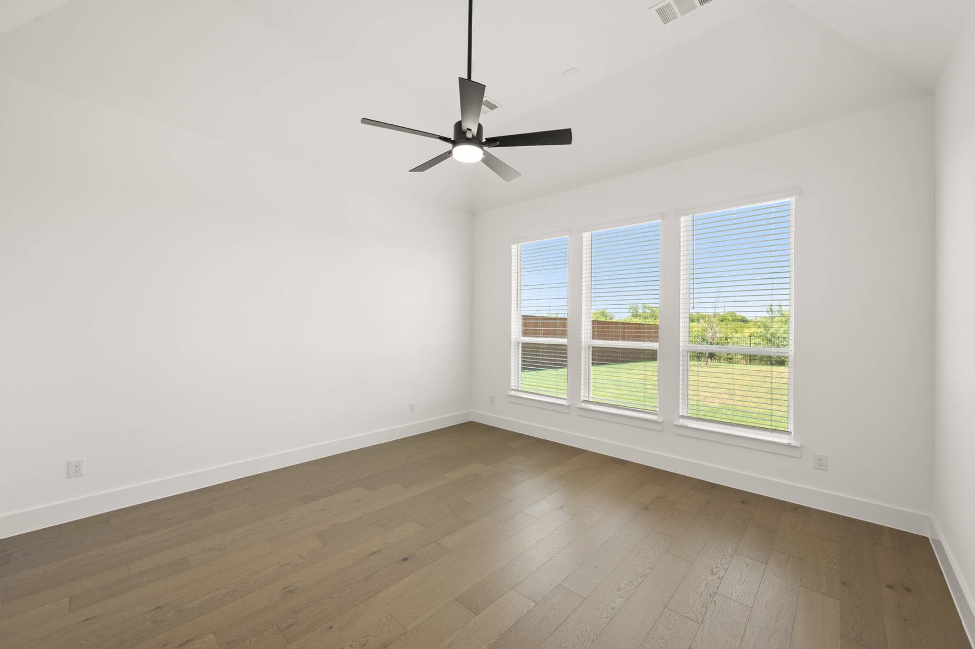 Spacious primary suite with hardwood floors and large windows overlooking the yard.