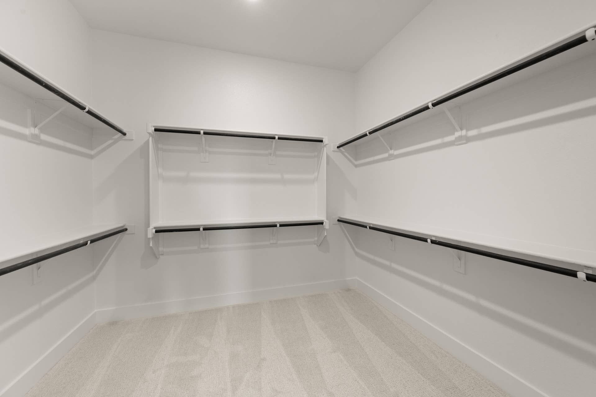 Spacious walk-in closet with multiple hanging rods and carpeted floor.