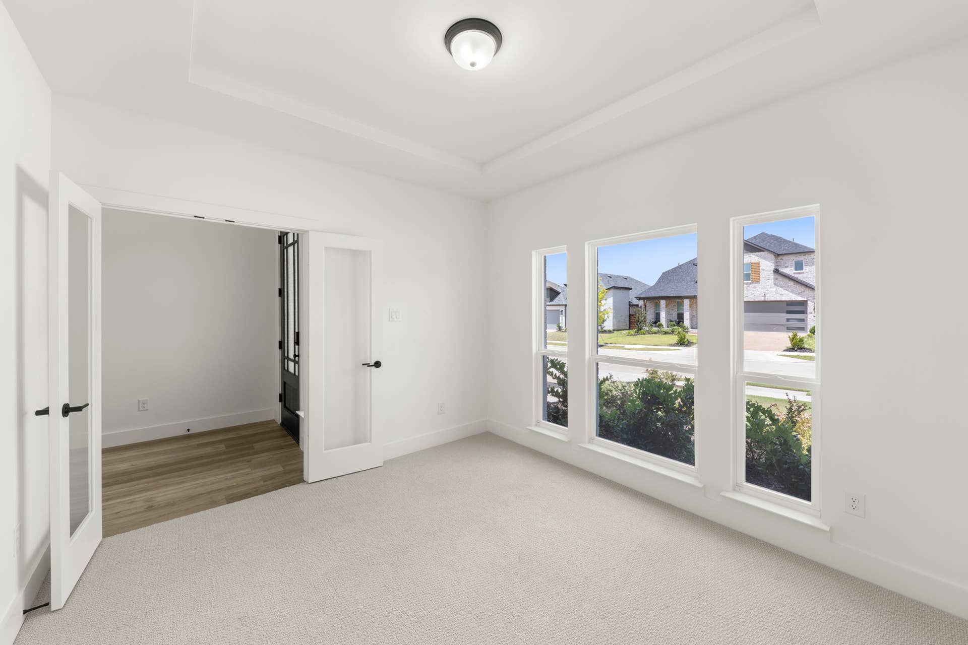 Bright study room with large windows and French doors, overlooking suburban street.