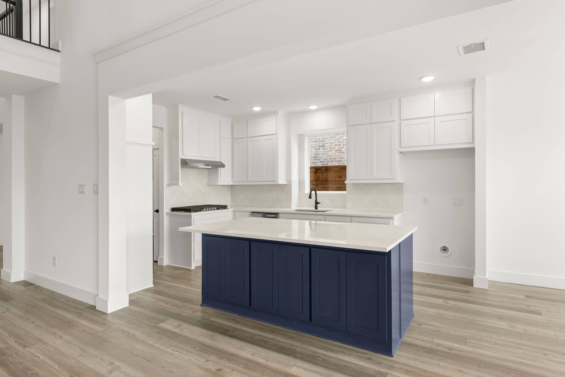 Modern kitchen with blue island, white cabinets, and wood flooring.