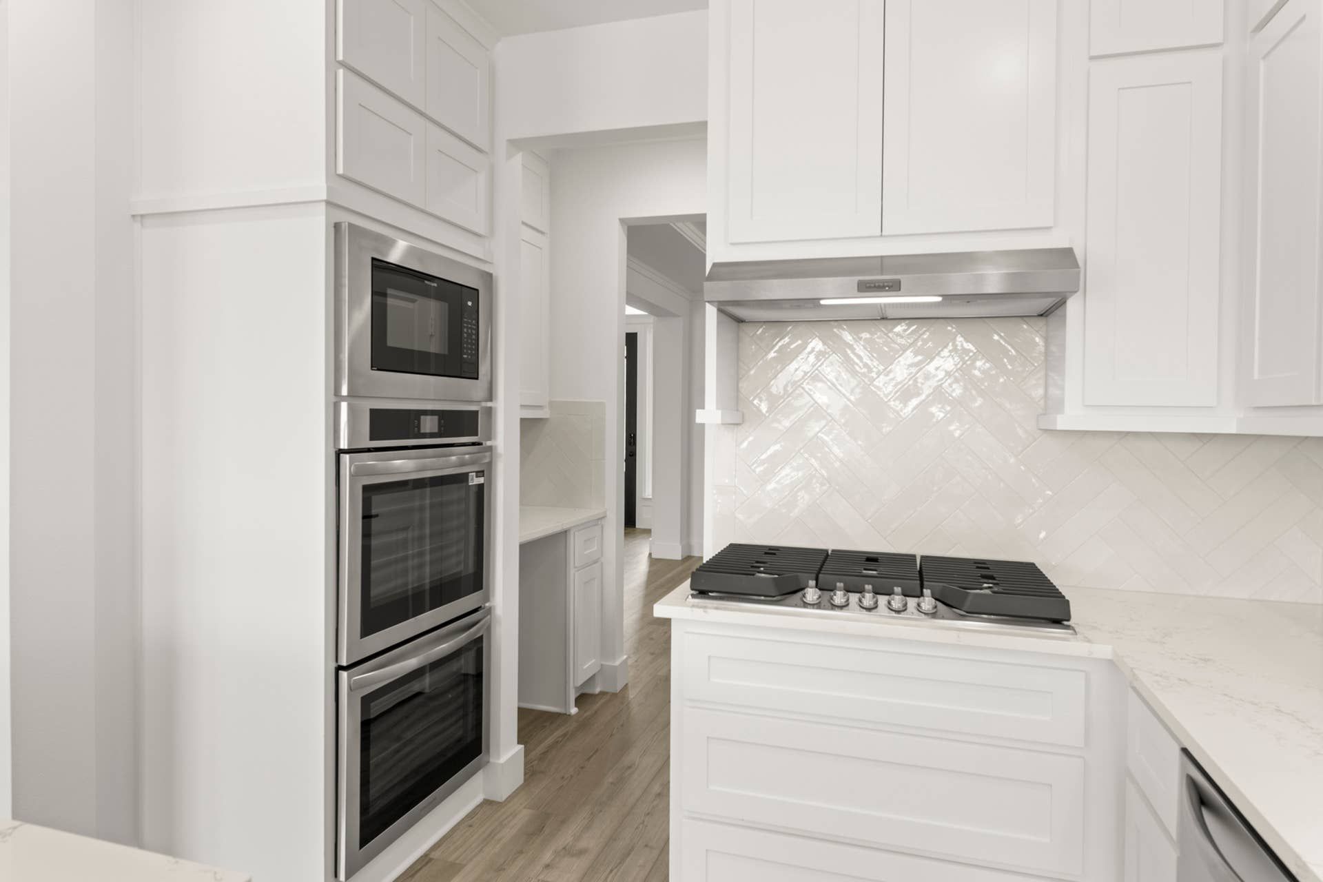 Modern kitchen with double ovens, gas cooktop, and herringbone tile backsplash.