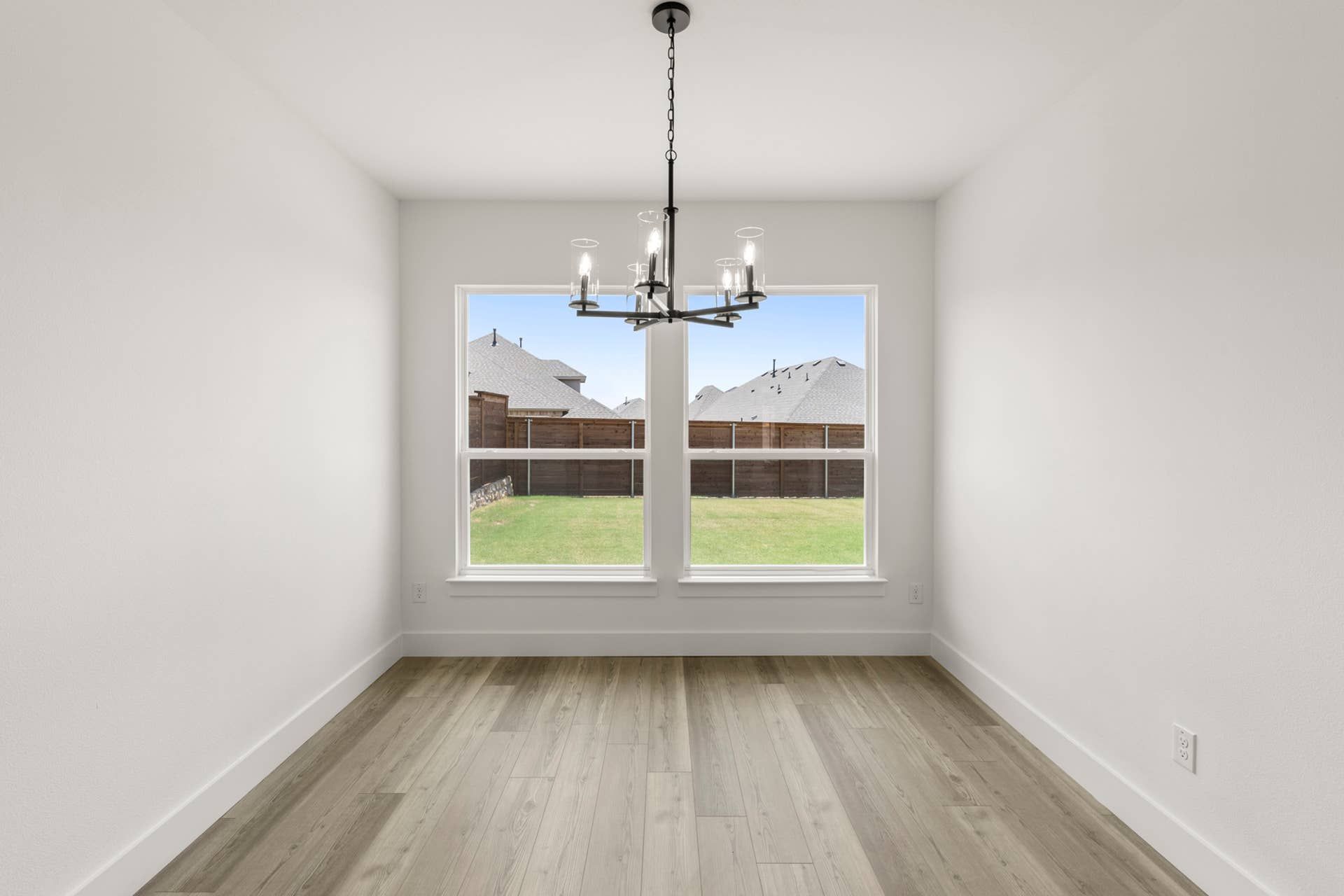 Bright dining nook with modern chandelier and large windows overlooking backyard.