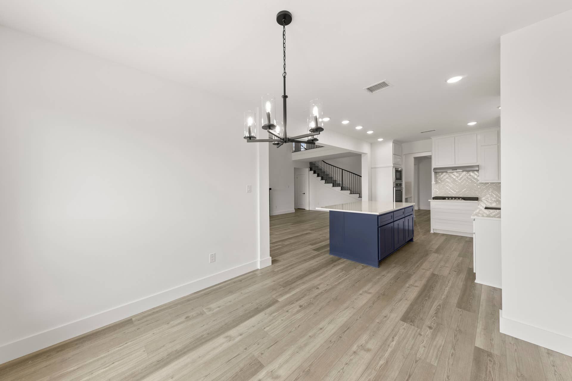 Spacious kitchen interior with navy island, modern chandelier, and wood flooring.