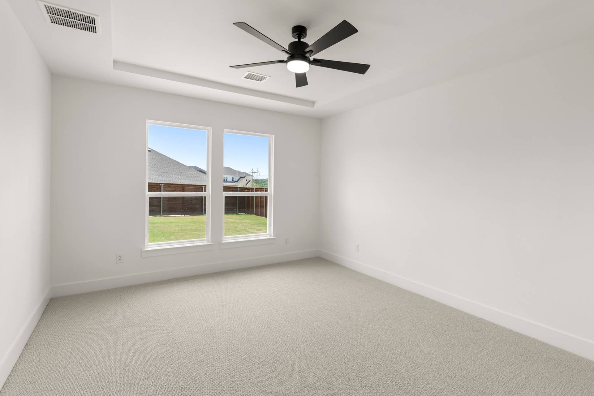 Bright bedroom with carpet, large windows, and ceiling fan.