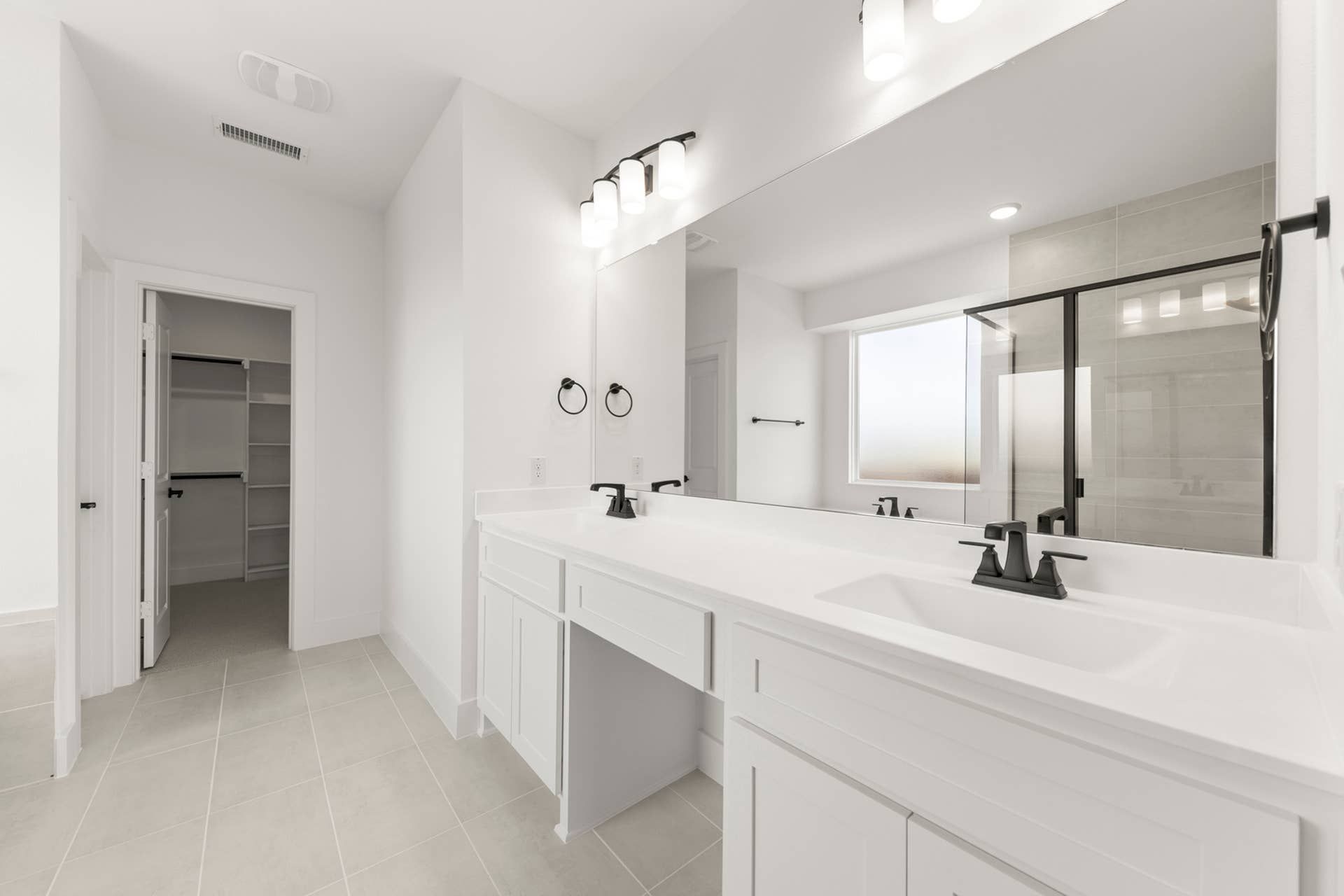 Spacious bathroom with double vanity, large mirror, and walk-in closet entrance.