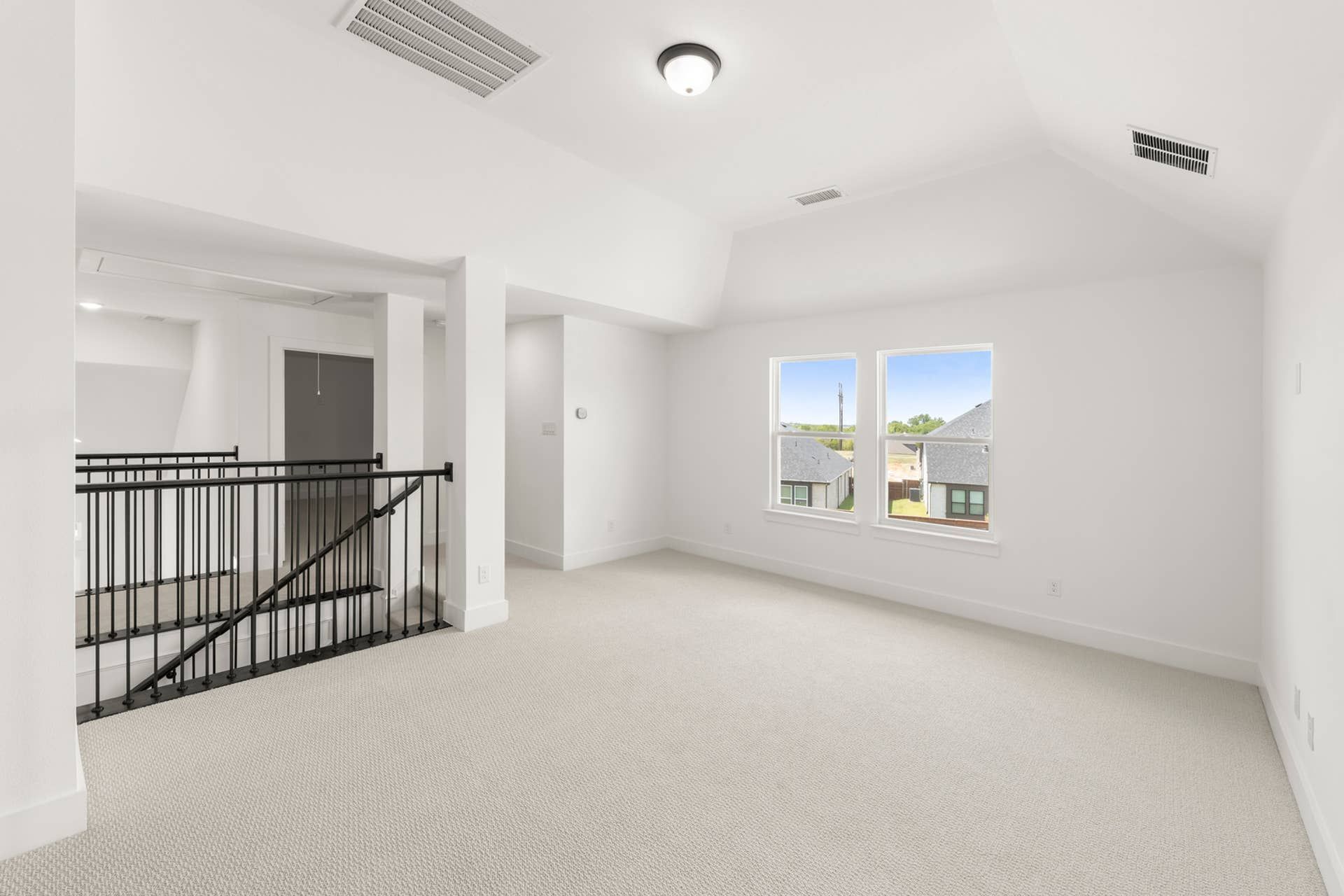 Spacious interior with carpeted floors, railing, and large windows overlooking rooftops.
