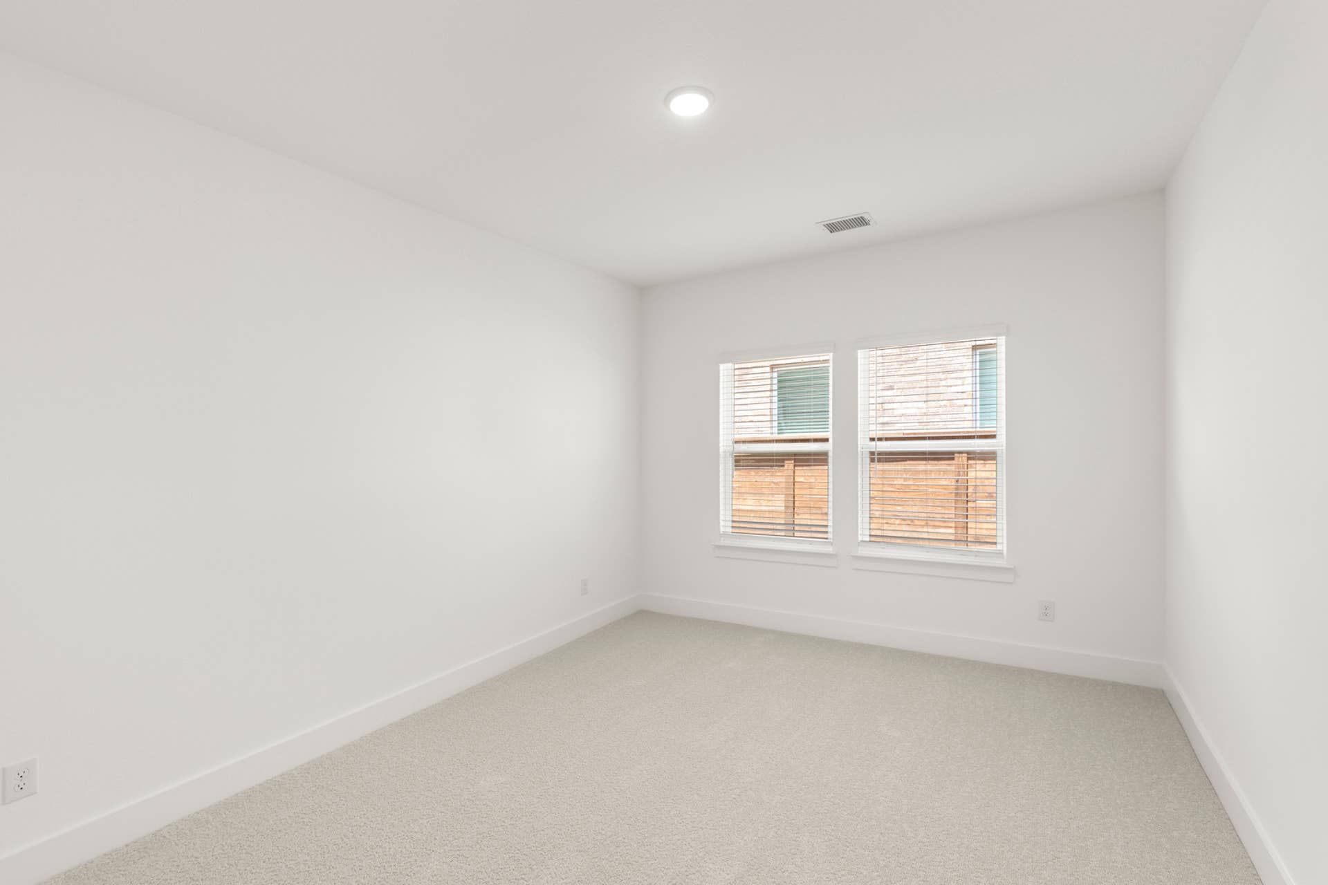 Bright, empty study room with two large windows and neutral carpet.