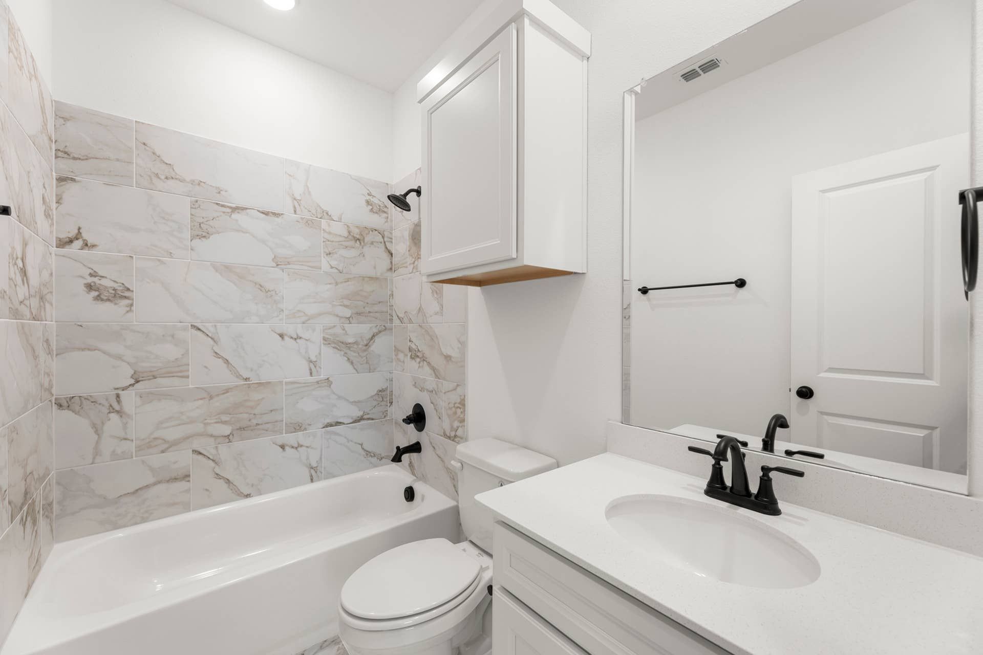 Modern bathroom with marble tile, white vanity, and black fixtures.