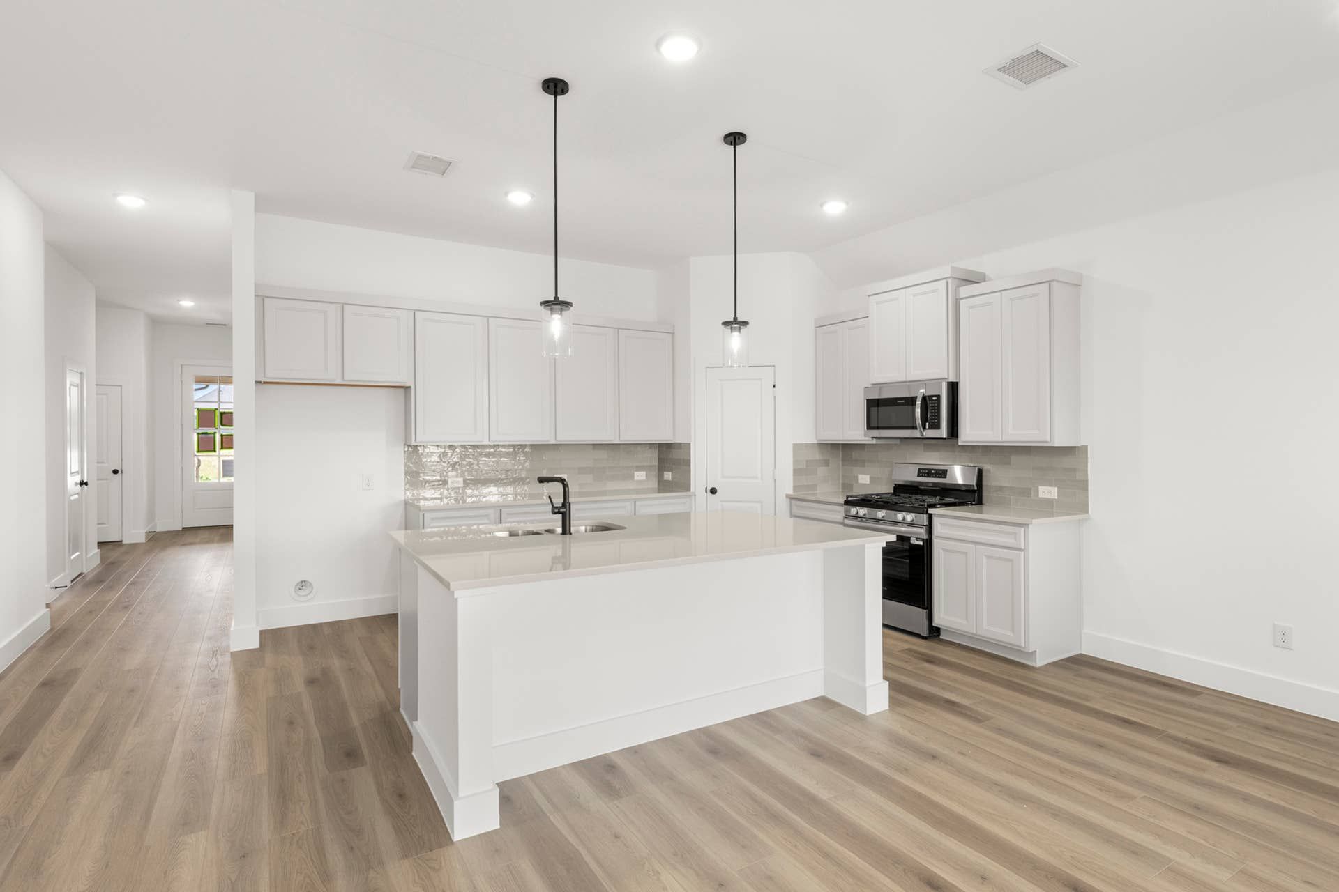 Modern kitchen with white cabinetry, island, pendant lights, and stainless steel appliances.