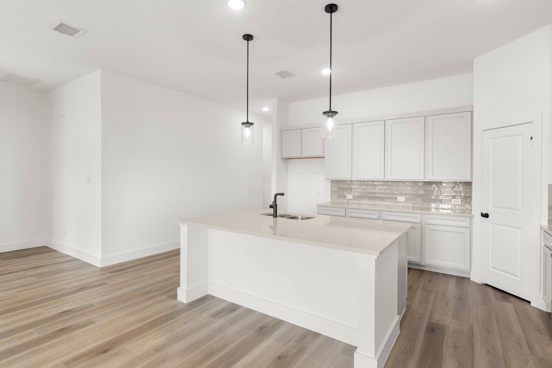 Modern kitchen with island, pendant lights, and wood flooring.