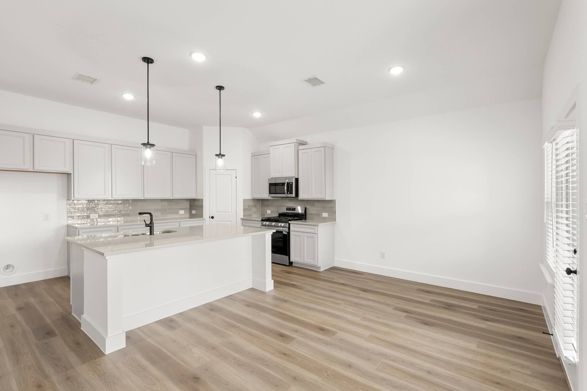 Modern kitchen with white cabinets, pendant lighting, and wood flooring.