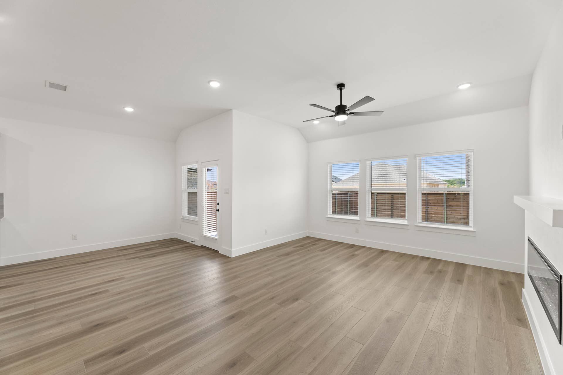 Spacious living room with wood flooring, ceiling fan, and large windows.