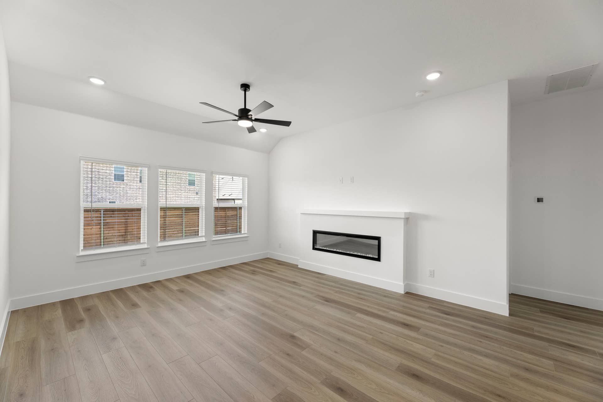 Spacious living room with modern fireplace and ceiling fan, featuring hardwood floors.