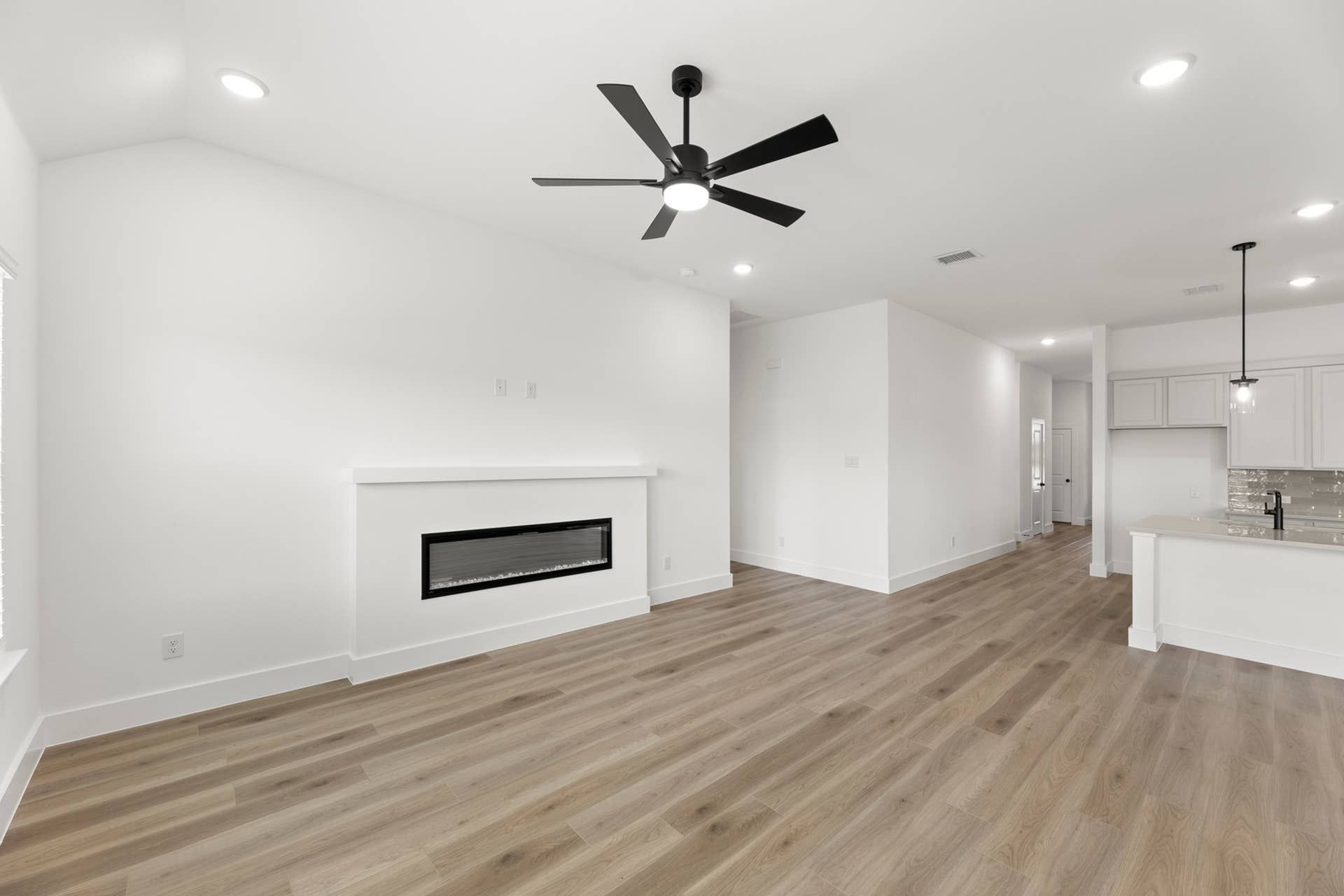 Spacious modern living area with ceiling fan, fireplace, and open kitchen.