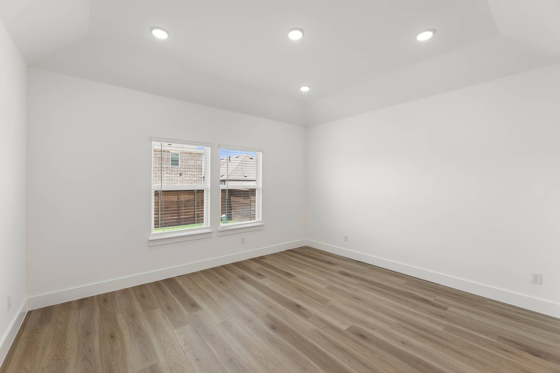 Minimalist empty room with recessed lighting and wood flooring.