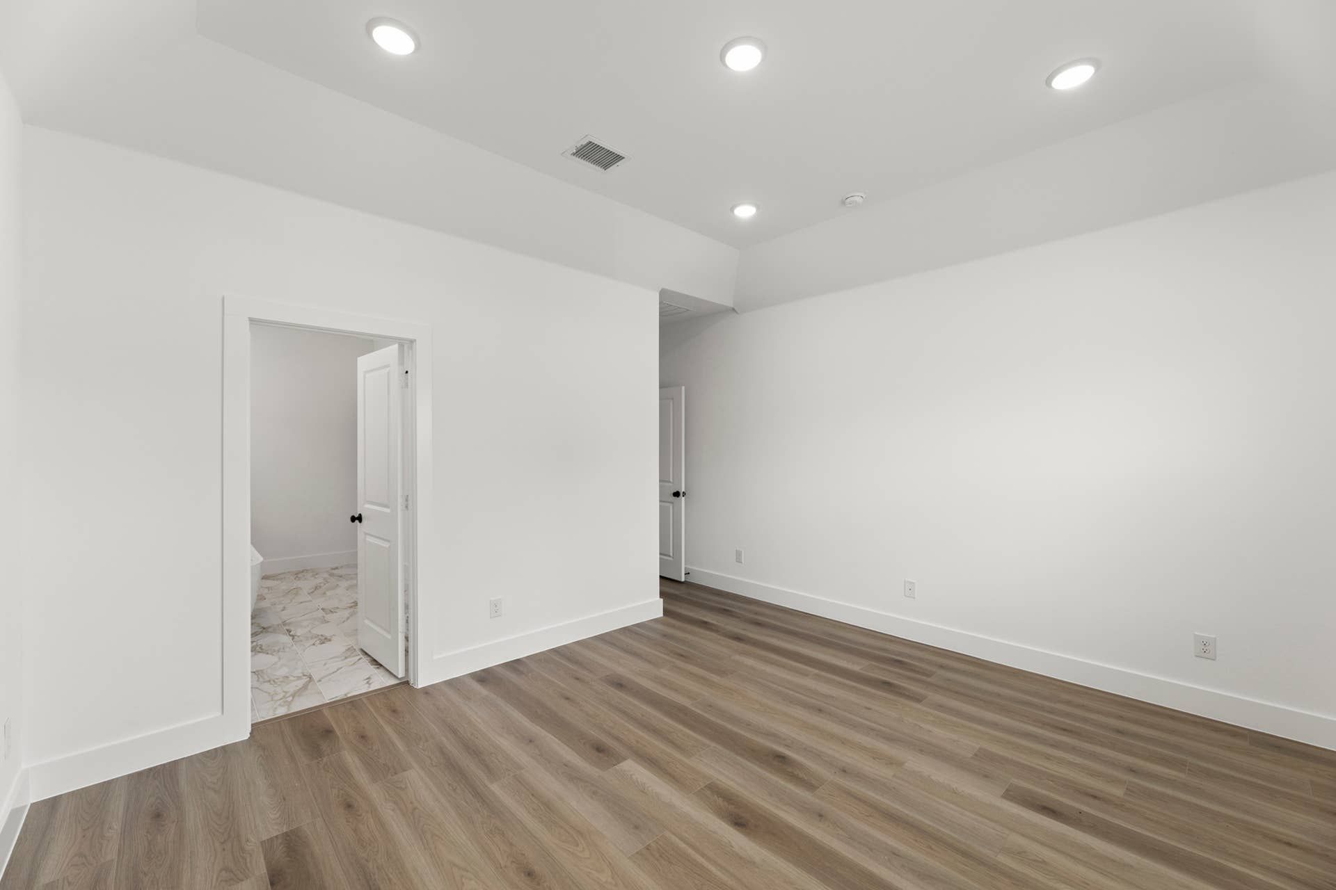 Modern interior with hardwood floors, recessed lighting, and adjacent tiled bathroom.