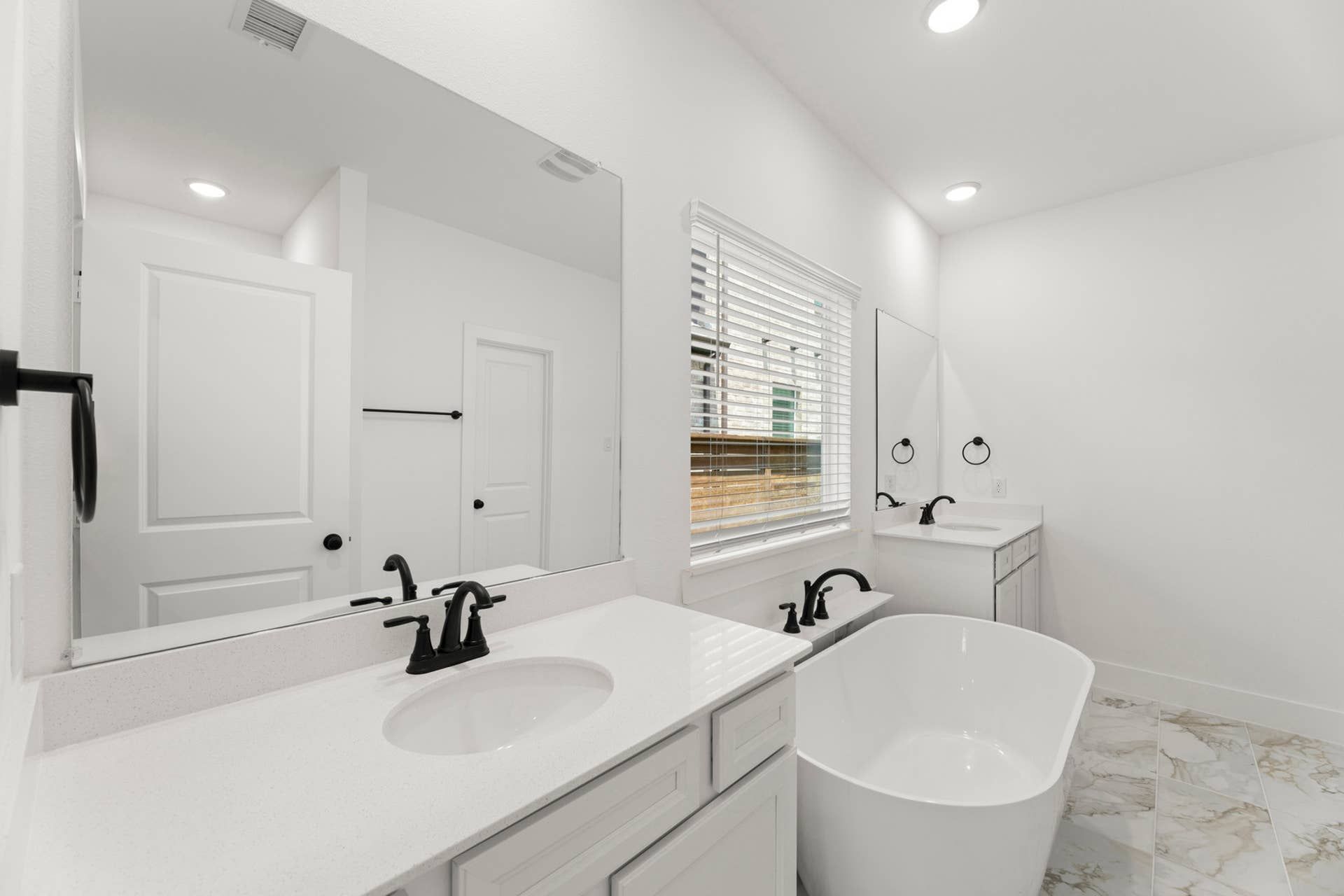 Bright bathroom with dual vanities, freestanding tub, and marble tile flooring.