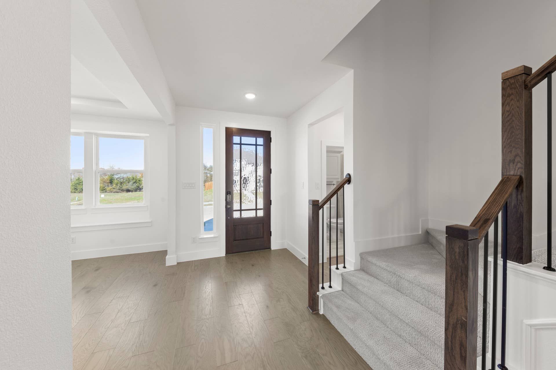 Bright entryway with wooden door, staircase, and hardwood floors.