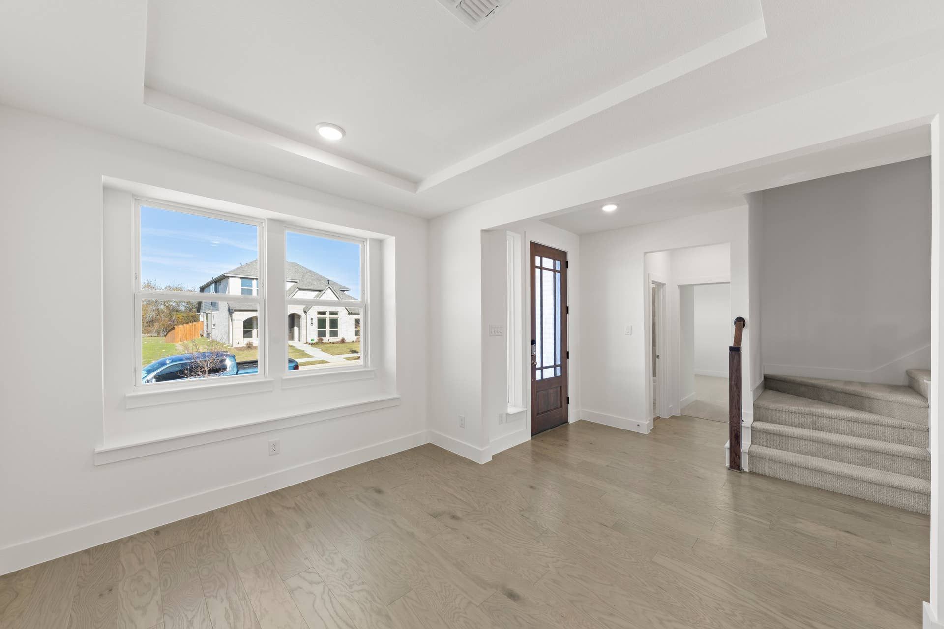 Bright interior with hardwood floors, large window, and staircase leading upstairs.