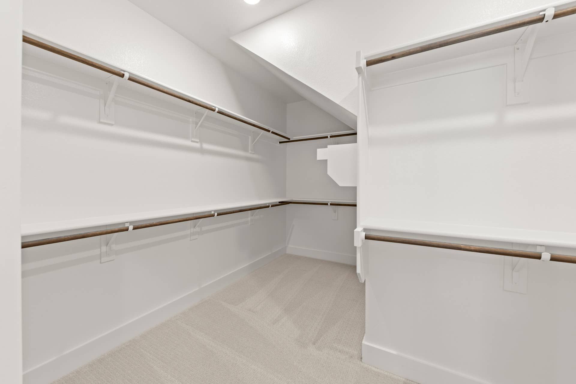 Spacious walk-in closet with wooden rods and white shelving.
