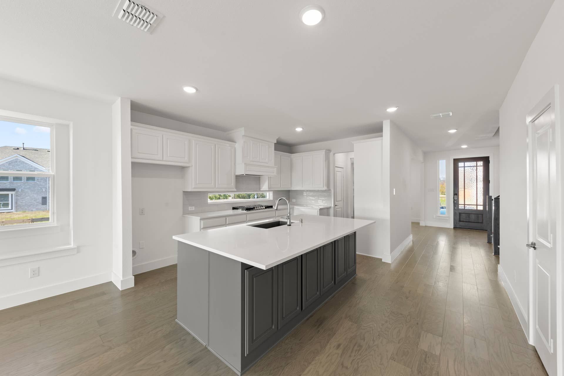 Modern kitchen with white cabinetry and central island, featuring hardwood floors.
