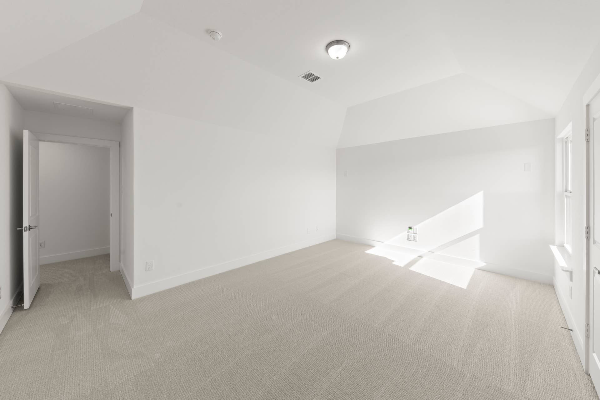 Spacious, sunlit empty room with beige carpet and white walls.