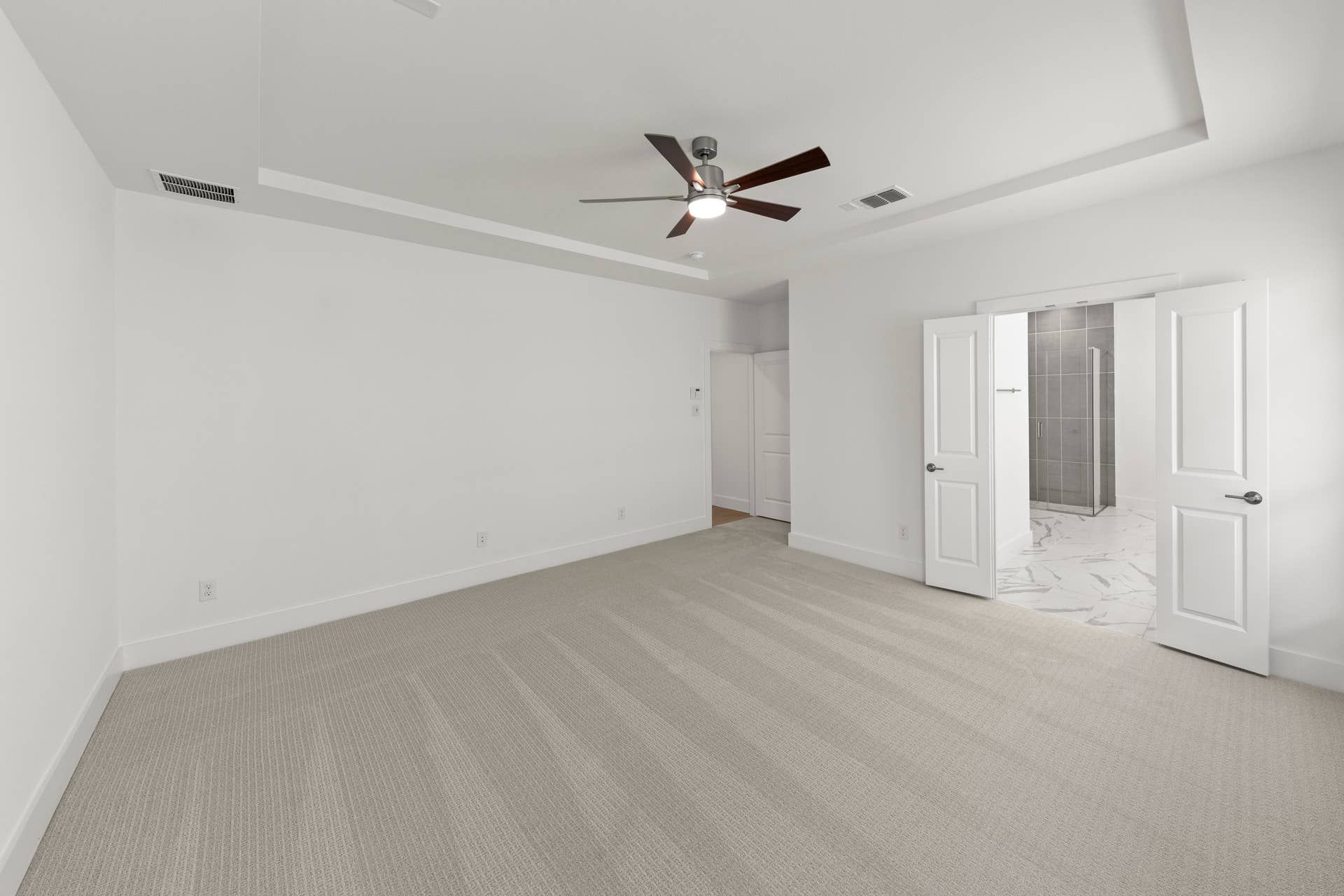 Spacious primary bedroom with carpet, ceiling fan, and en-suite bathroom entrance.