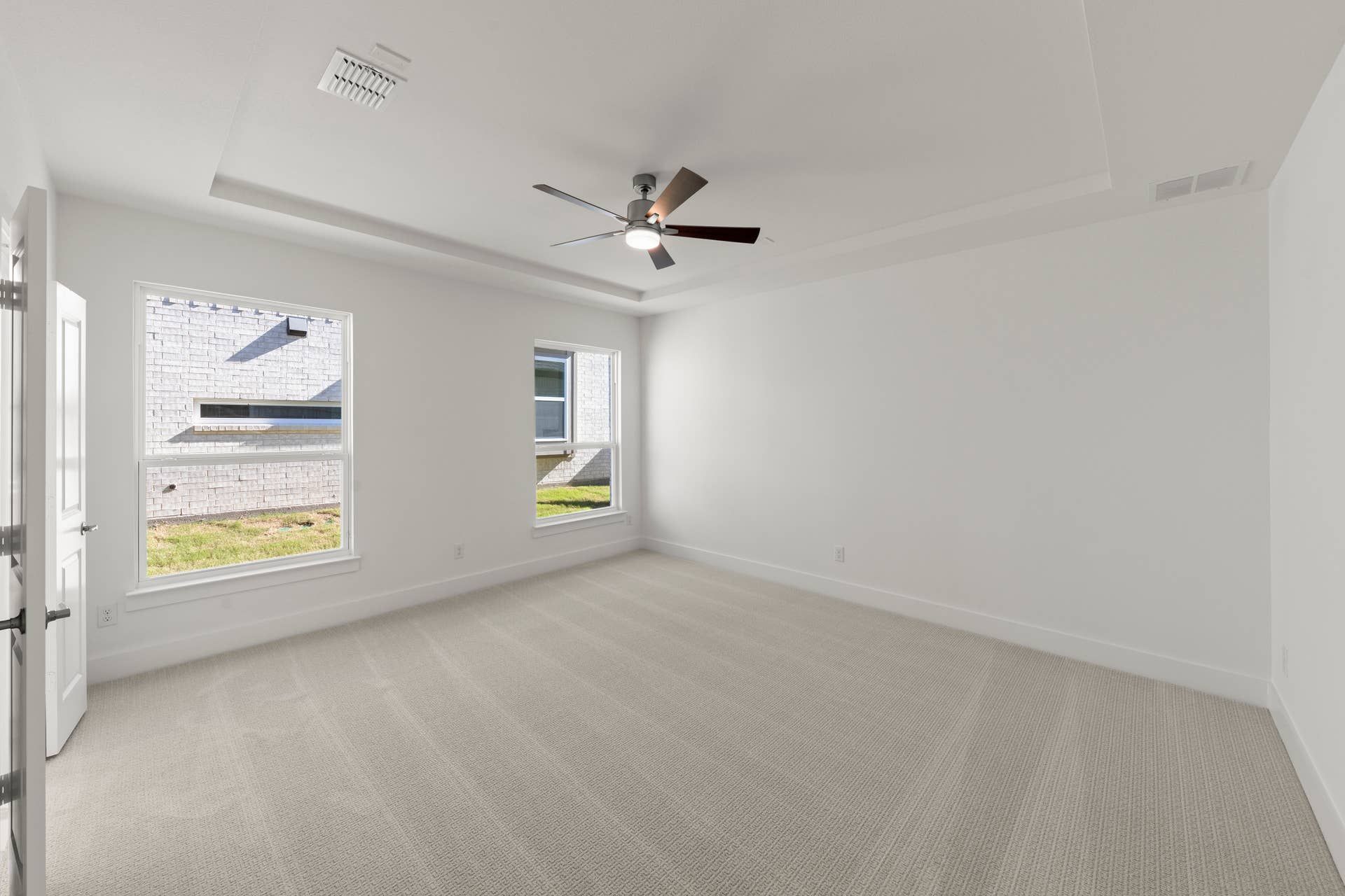 Spacious bedroom with tray ceiling, carpet flooring, and large windows.