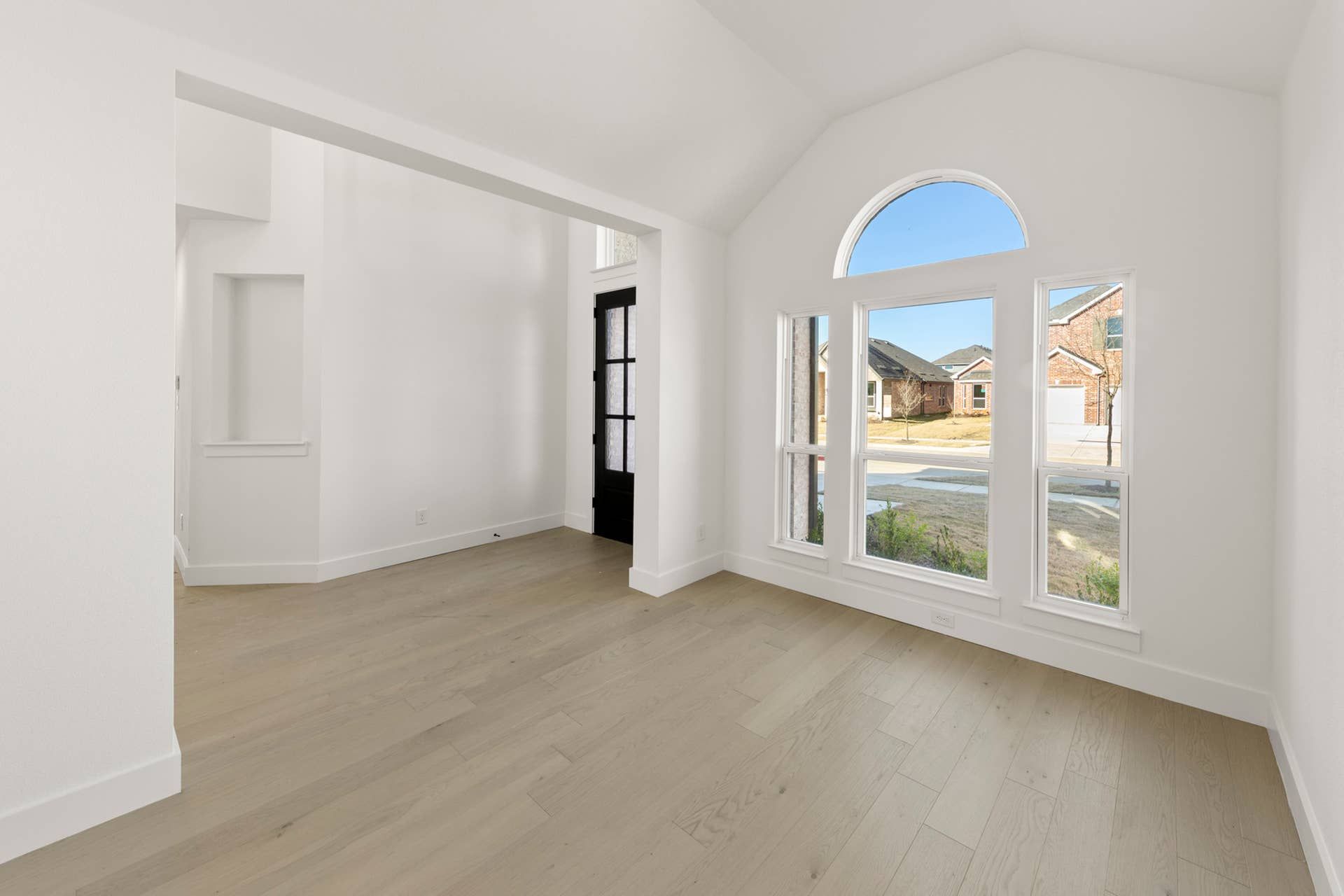 Bright dining room with arched window and light wood flooring.