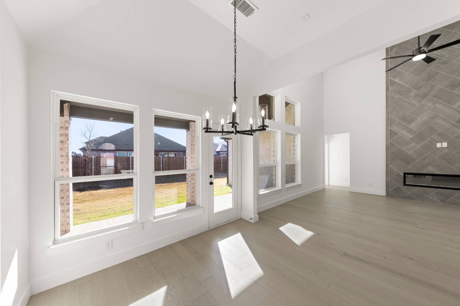 Spacious living area with large windows, modern chandelier, and tiled fireplace wall.