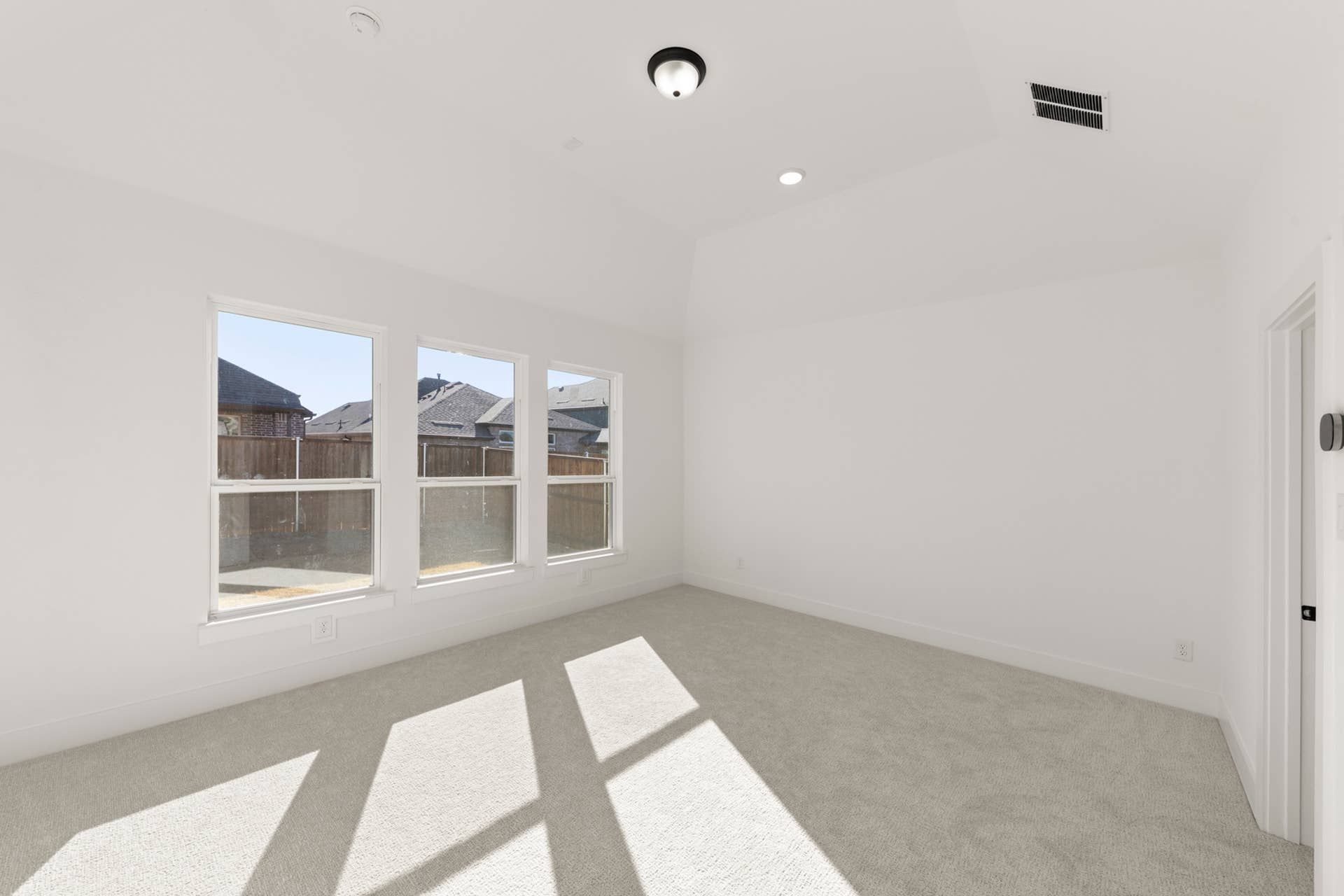 Bright empty room with large windows and light carpet flooring.