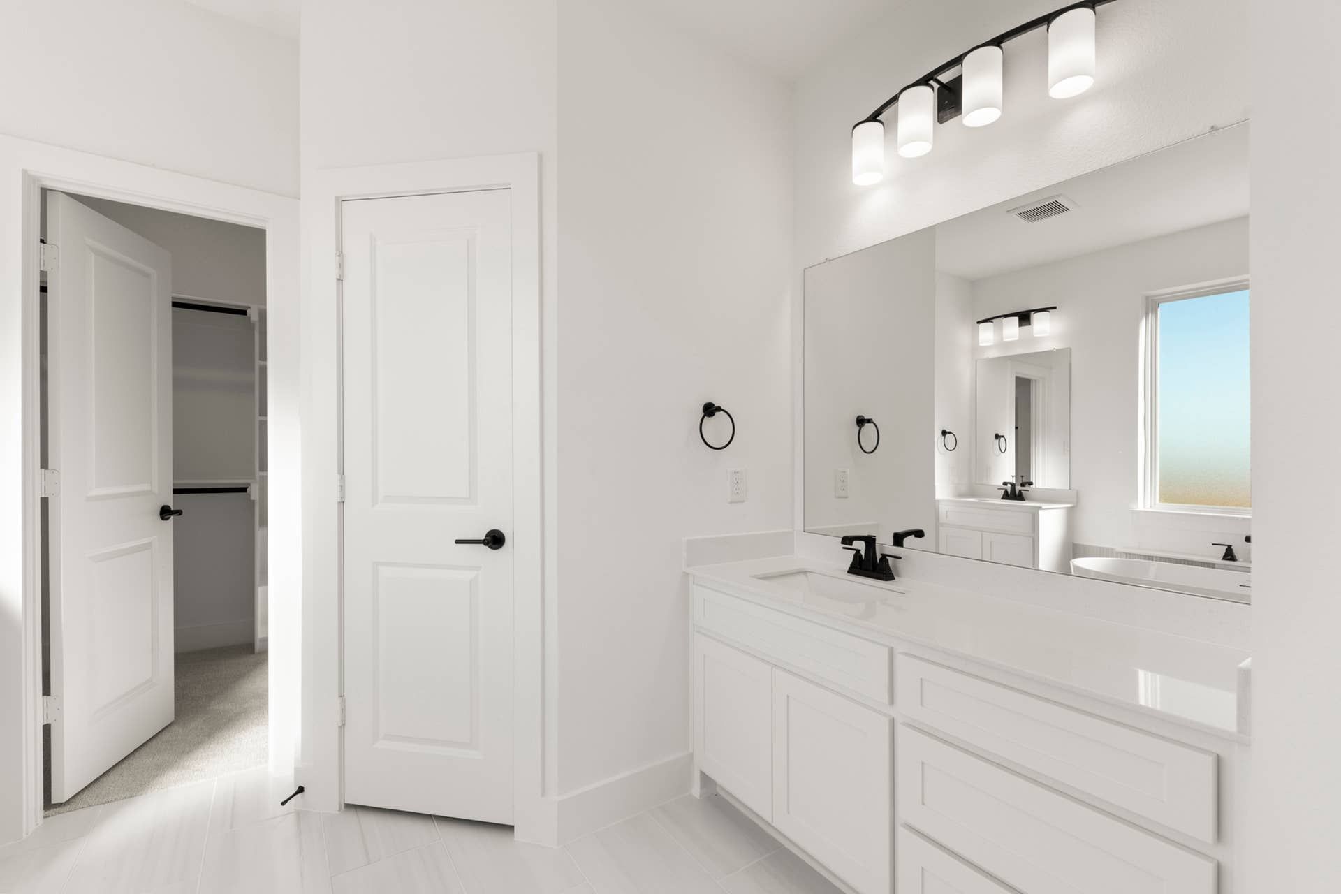 Modern bathroom with dual sinks, large mirror, and white cabinetry.