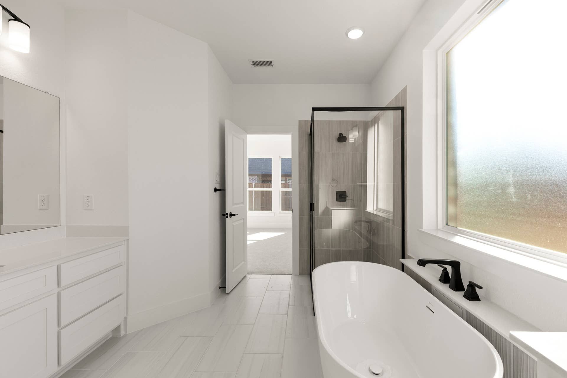 Modern bathroom with freestanding tub, glass shower, and large frosted window.