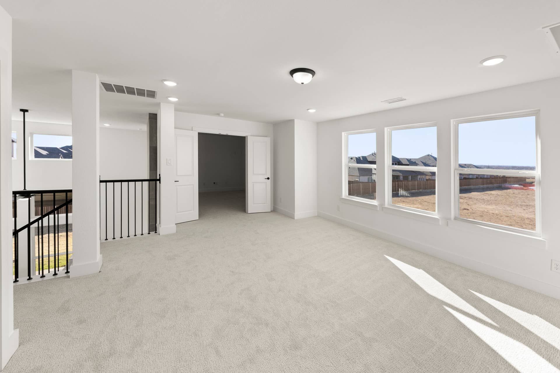Spacious carpeted room with large windows and double doors, overlooking suburban landscape.