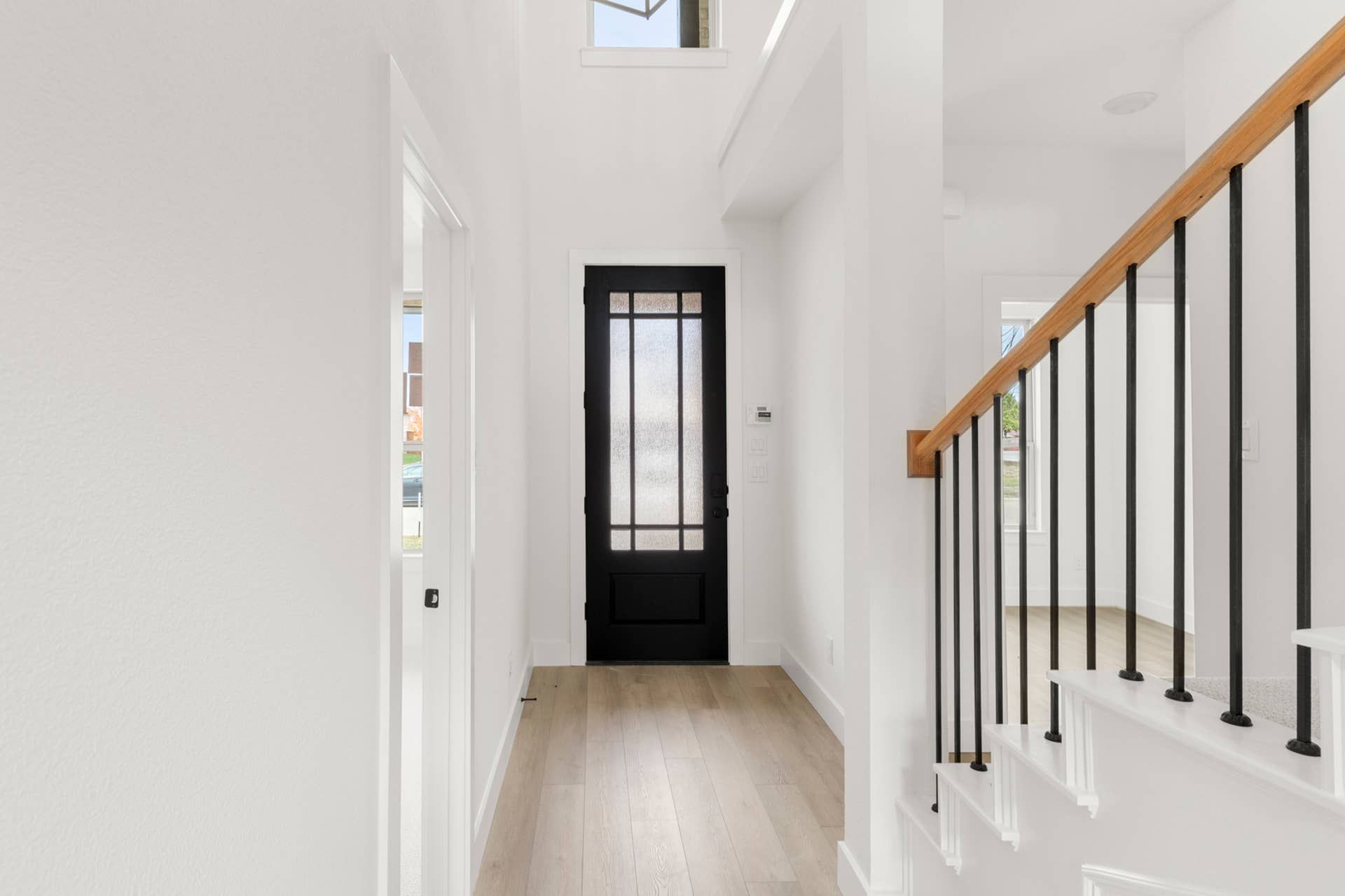 Bright modern entryway with black door and wooden staircase.