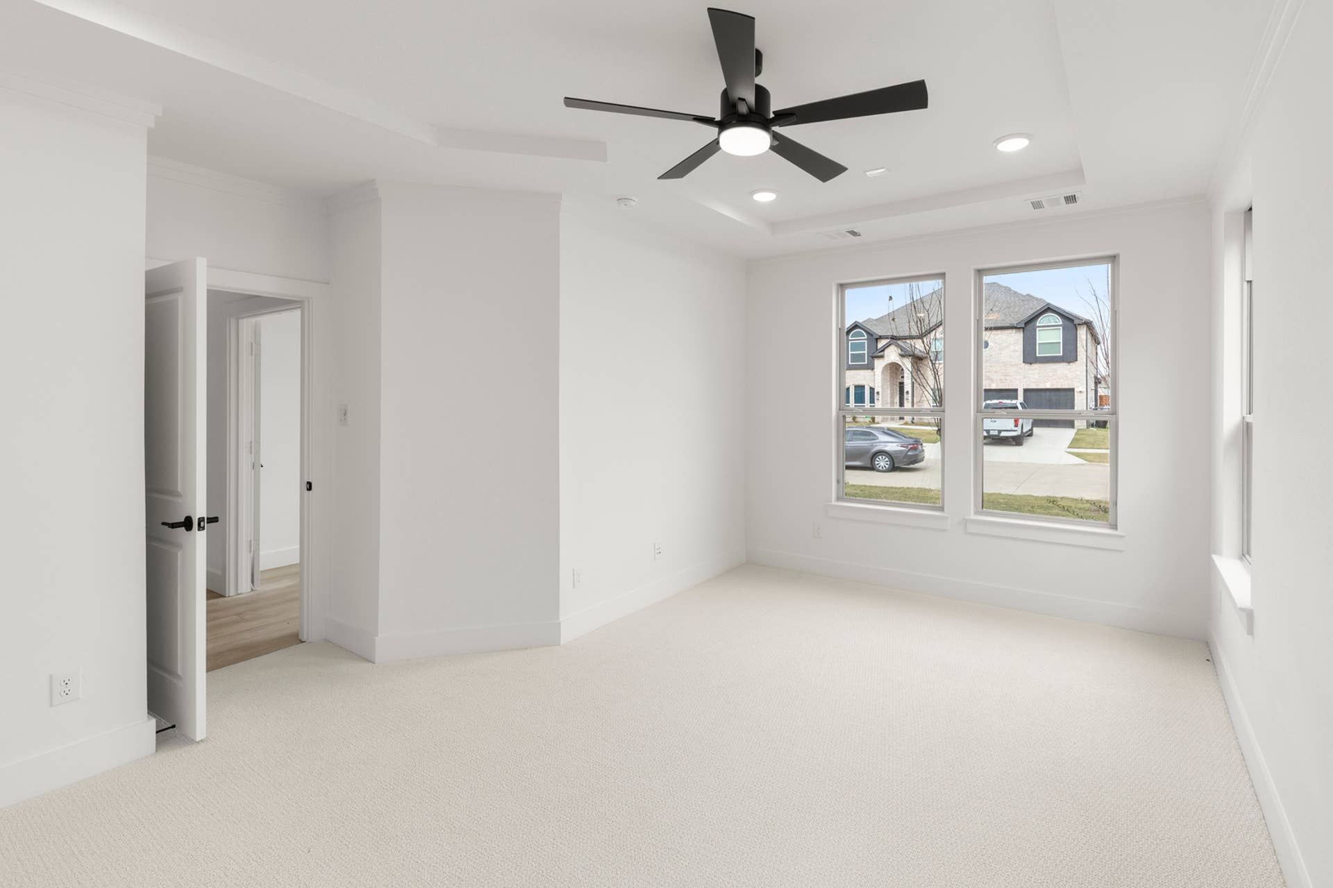 Bright room with ceiling fan, two large windows, and open door.