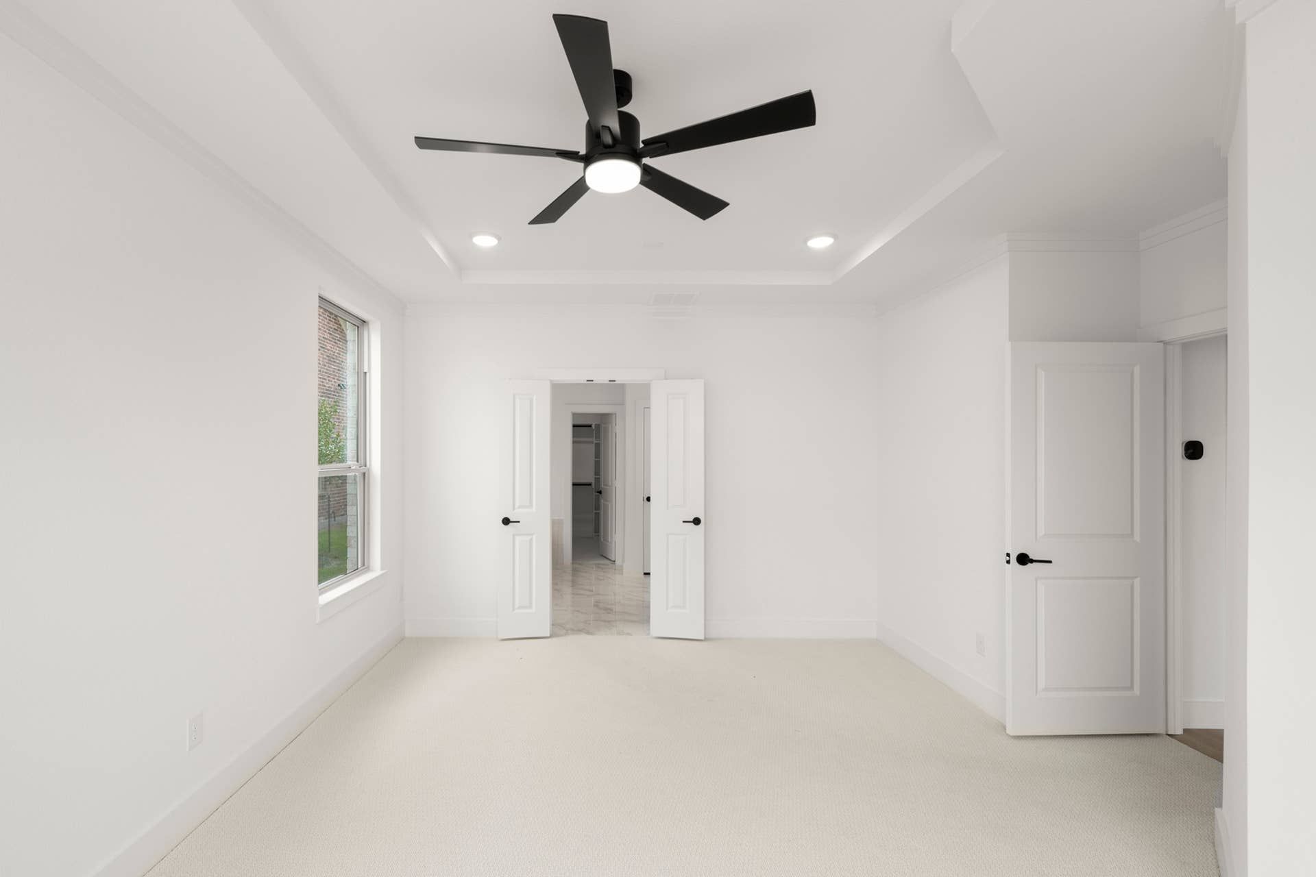 Spacious white bedroom with modern ceiling fan and double doors.