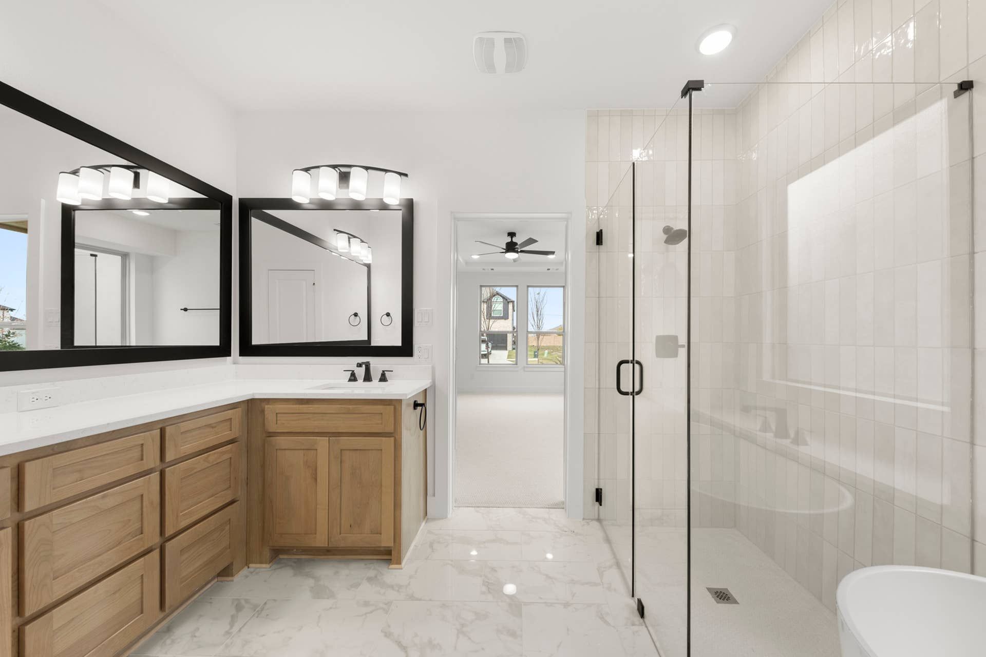 Modern bathroom with glass shower, dual mirrors, and wooden cabinetry.