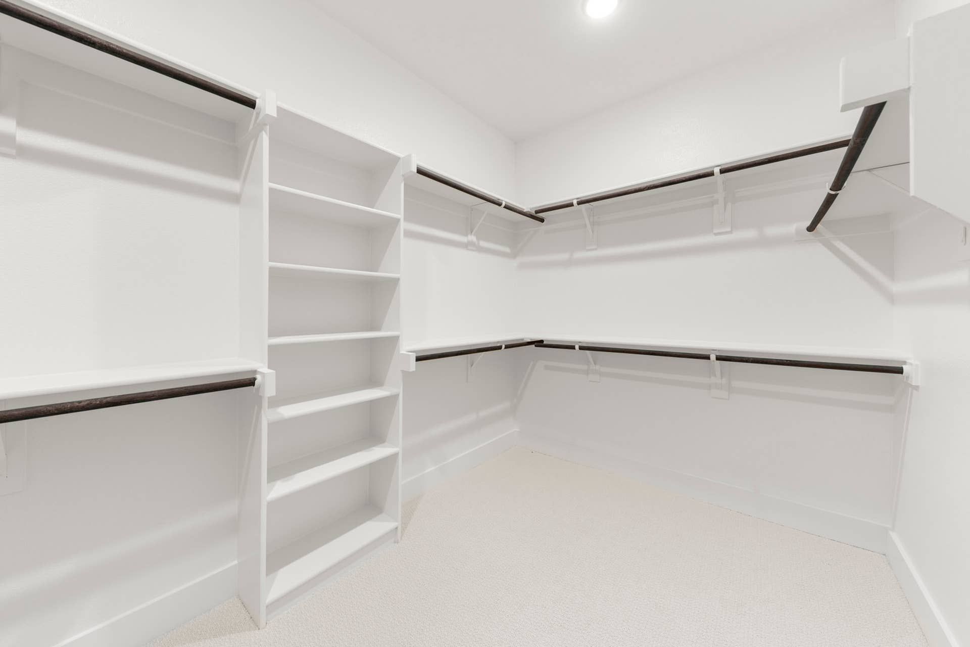 Spacious walk-in closet with white shelving and dark wooden rods.