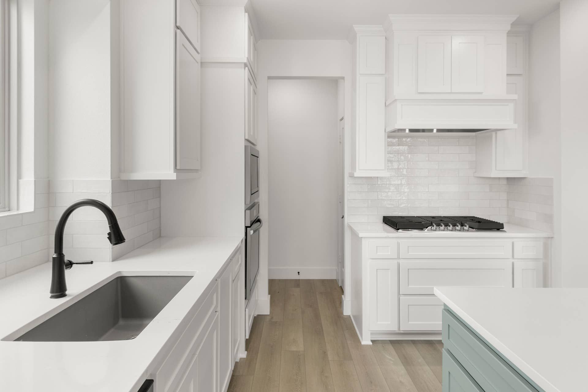 Modern kitchen with white cabinetry, black faucet, and light wood flooring.